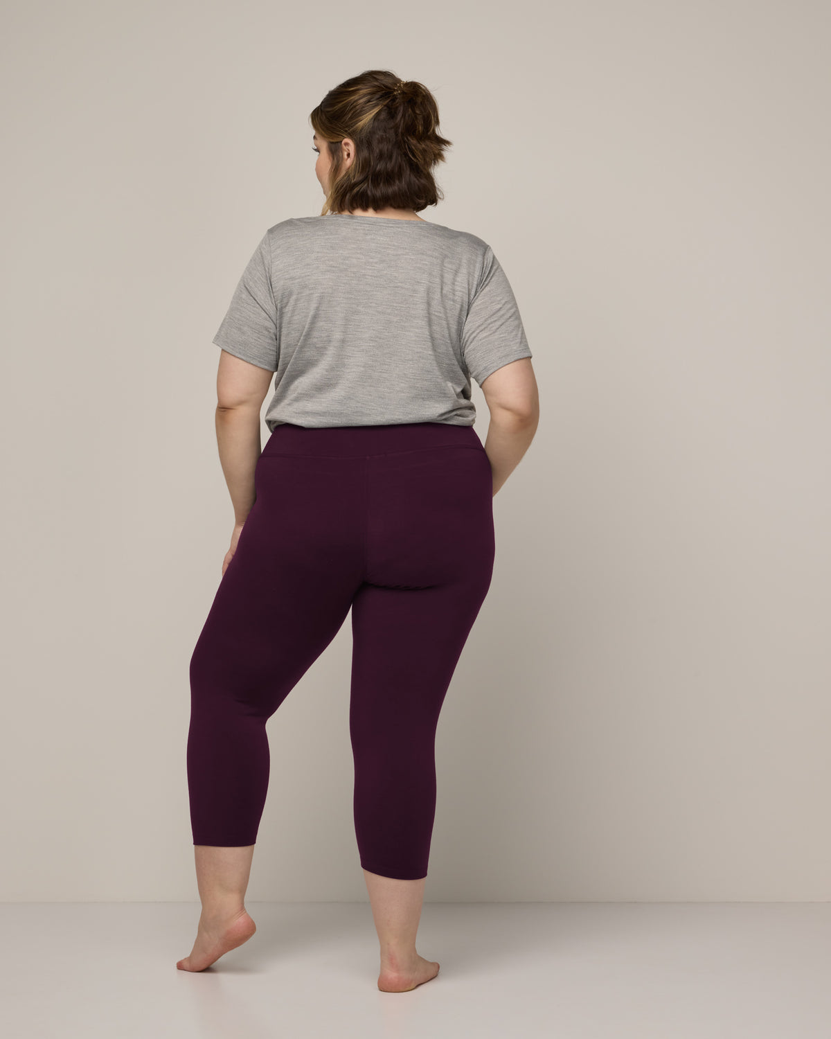 Model wearing Summit Crop Legging in Dark Marionberry, a deep berry purple color. Summit Crop Legging is a merino wool legging available in sizes XS-3X.