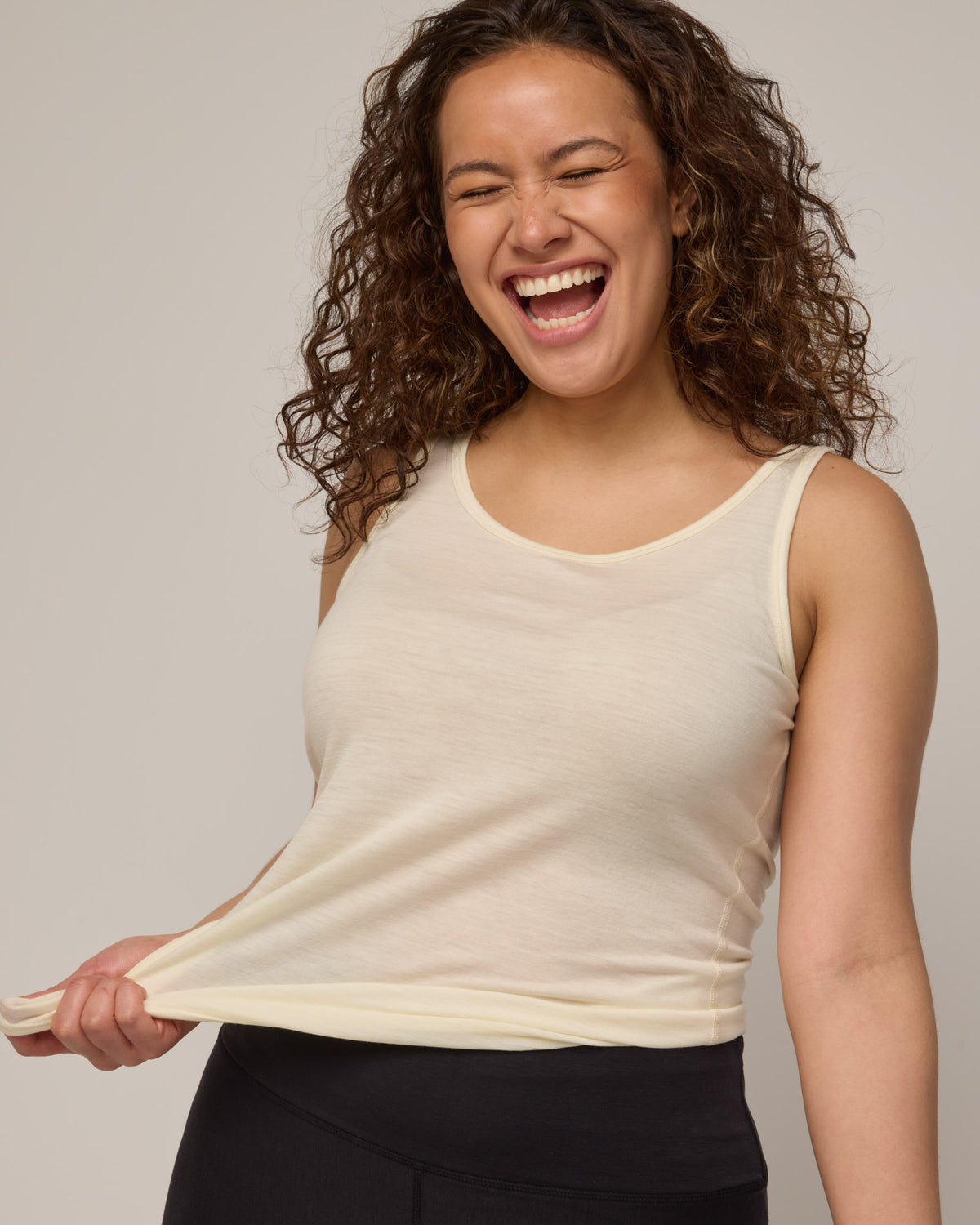 Model wearing Essential Layering Tank in Natural White, an off-white cream color. Essential Layering Tank is a merino wool sleeveless, reversible, slim fit top available in sizes XS-3X.