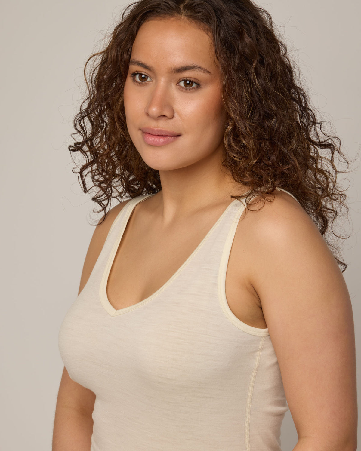 Model wearing Essential Layering Tank in Natural White, an off-white cream color. Essential Layering Tank is a merino wool sleeveless, reversible, slim fit top available in sizes XS-3X.