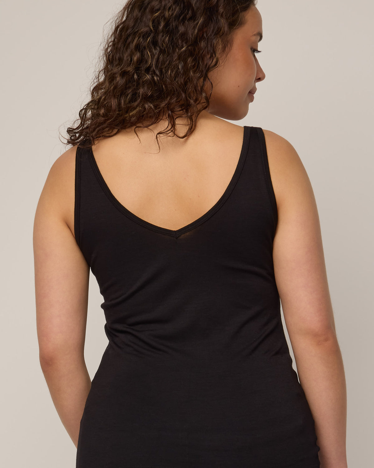 Model wearing Essential Layering Tank in Black. Essential Layering Tank is a merino wool sleeveless, reversible, slim fit top available in sizes XS-3X.
