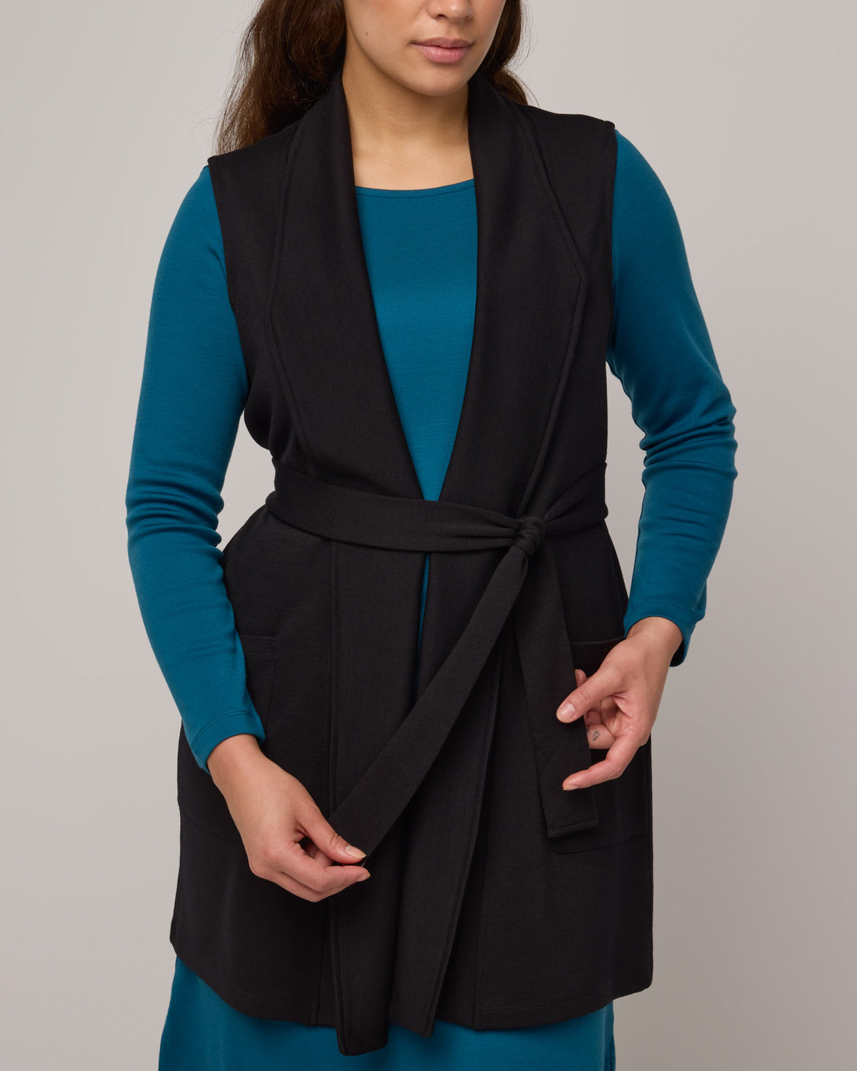 Model wearing Dylan Belted Vest in Black. Dylan Belted Vest is a merino wool sleevelessvest with pockets available in sizes XS-3X.