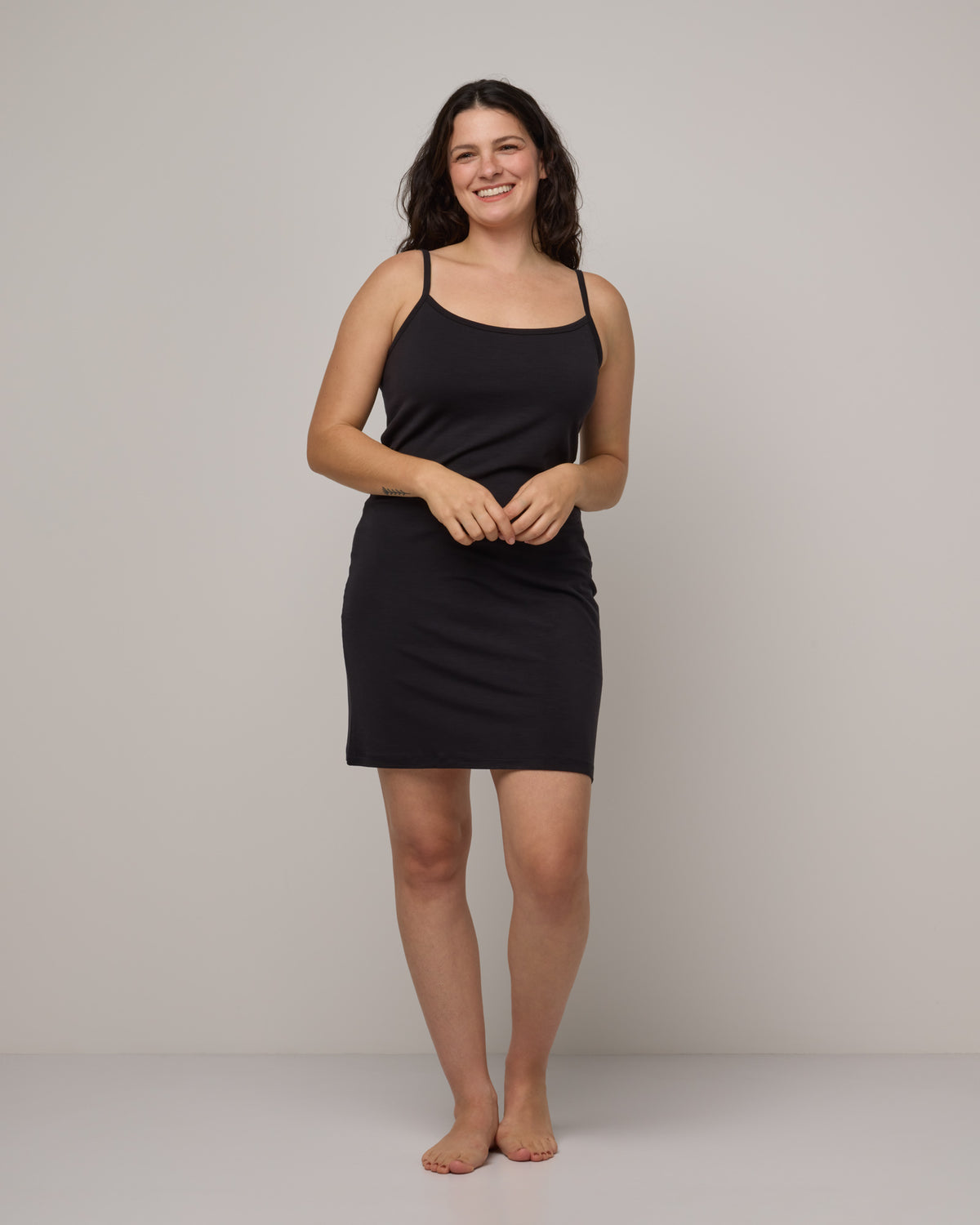 Model wearing Roam Cami Slip in Black. Roam Cami Slip is a merino wool sleeveless, scoop neck, knee length fitted underwear available in sizes XS-3X.