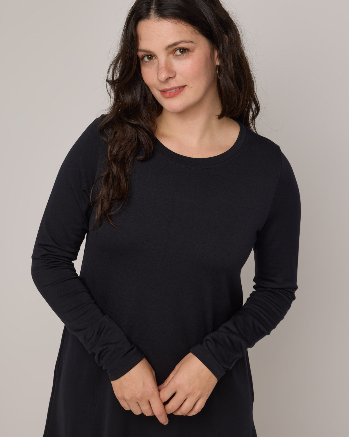 Model wearing Eliza Swing Dress in Black. Eliza Swing Dress is a merino wool long sleeve, crew neck, knee length swing dress with pockets available in sizes XS-3X Regular, XS-3X Long.