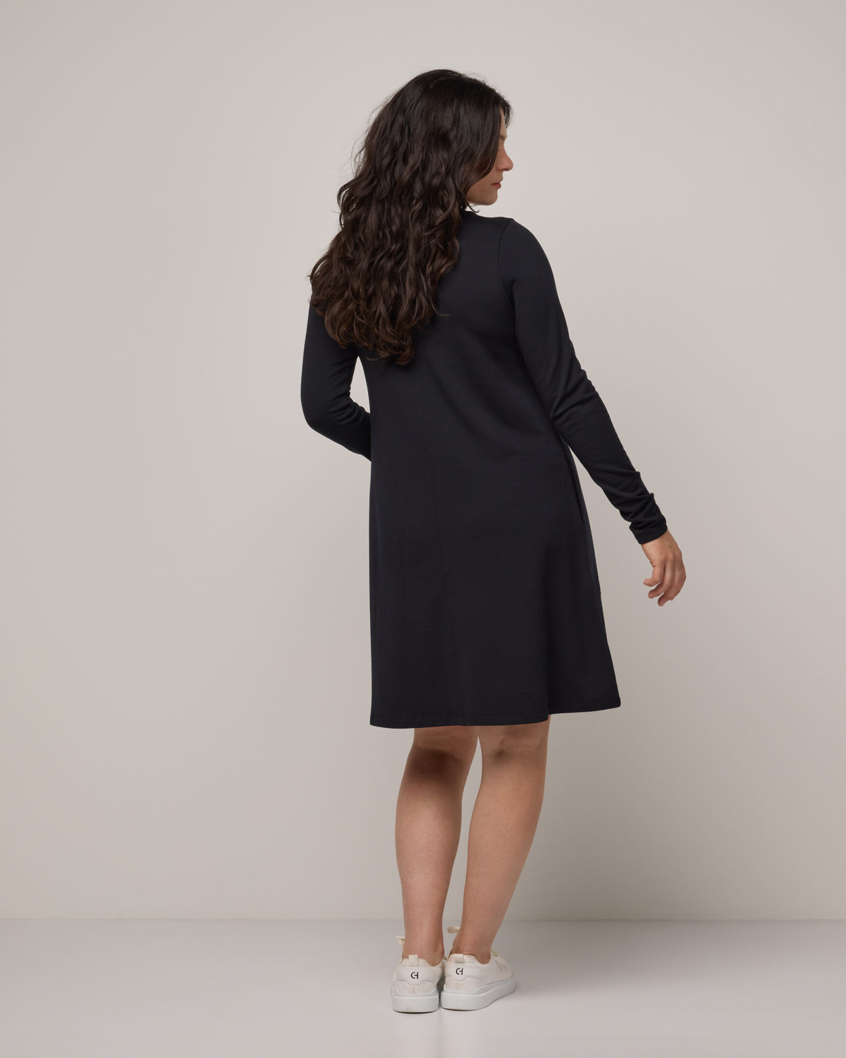 Model wearing Eliza Swing Dress in Black. Eliza Swing Dress is a merino wool long sleeve, crew neck, knee length swing dress with pockets available in sizes XS-3X Regular, XS-3X Long.