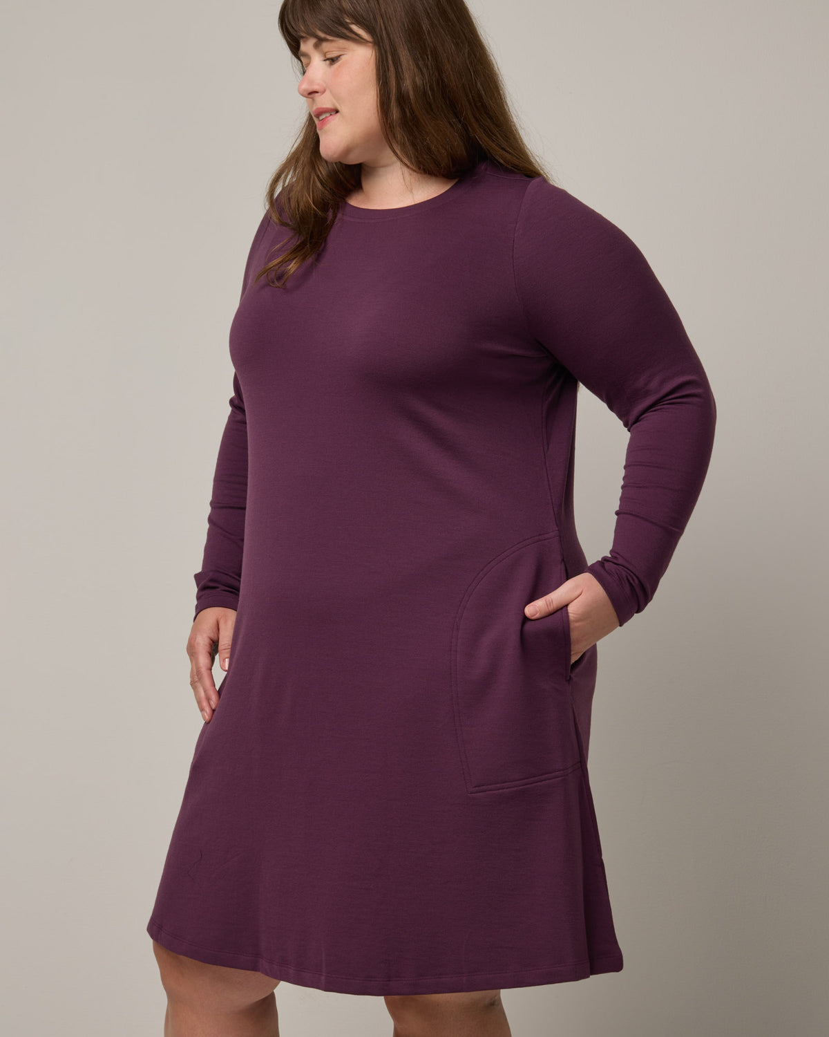 Model wearing Eliza Swing Dress in Marionberry, a dark berry purple color. Eliza Swing Dress is a merino wool long sleeve, crew neck, knee length swing dress with pockets available in sizes XS-3X Regular, XS-3X Long.