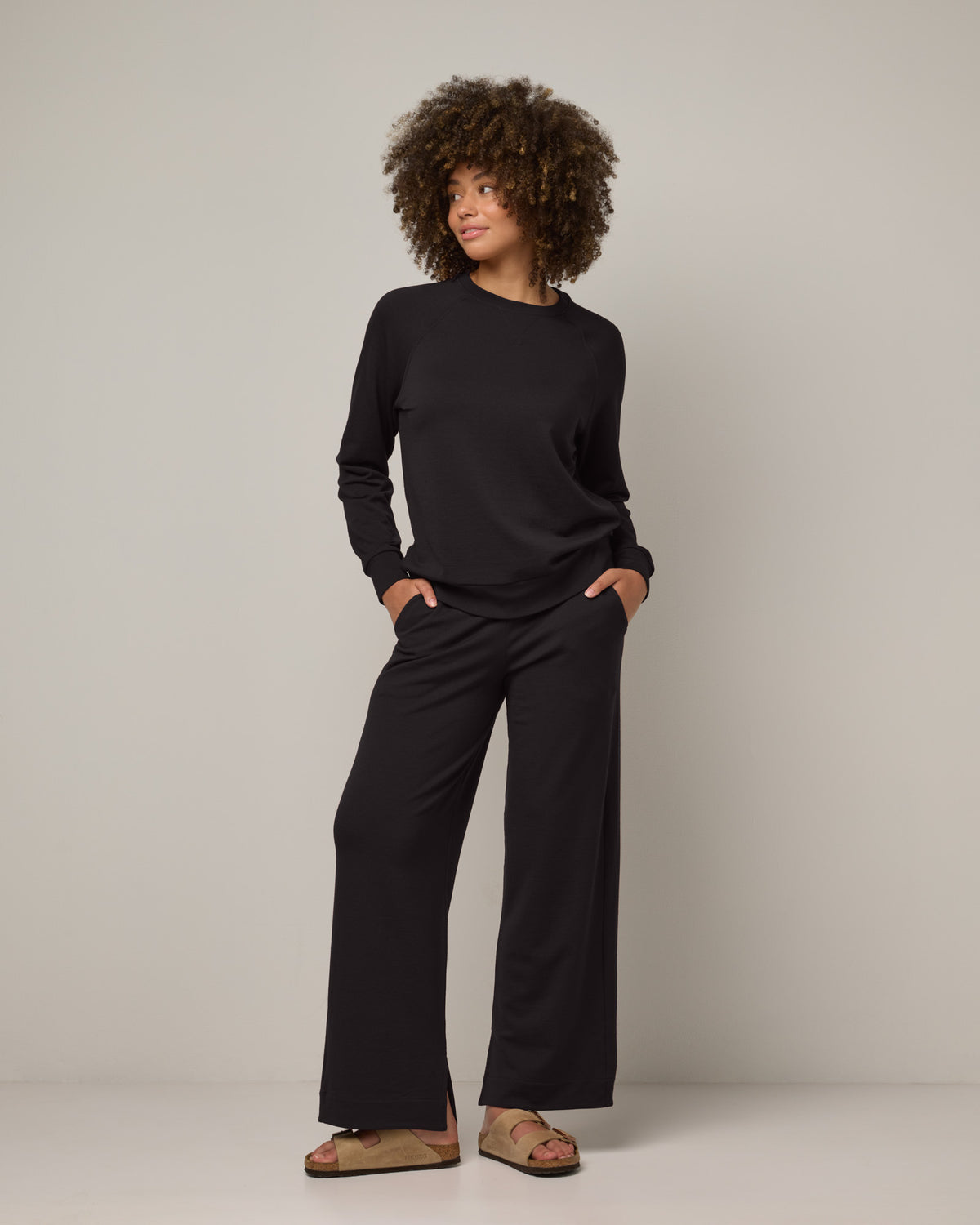 Model wearing Aspen Wide Leg Sweatpants in Black. Aspen Wide Leg Sweatpants is a merino wool sweatpant with pockets available in sizes XS-3X.