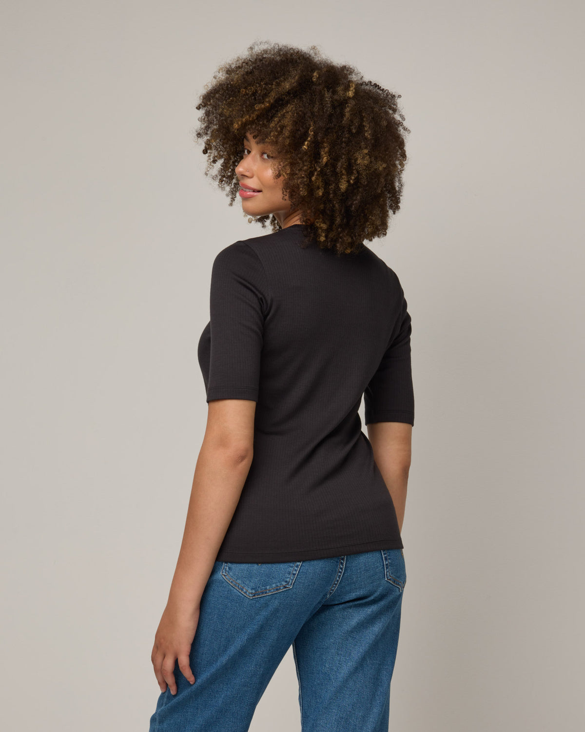 Model wearing Celine Ribbed Elbow Sleeve Tee in Black. Celine Ribbed Elbow Sleeve Tee is a merino wool short sleeve, scoop neck, slim fit tee available in sizes XS-3X.