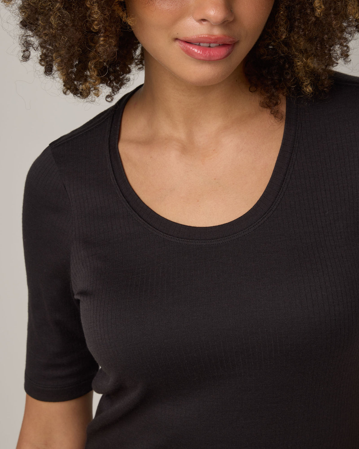 Model wearing Celine Ribbed Elbow Sleeve Tee in Black. Celine Ribbed Elbow Sleeve Tee is a merino wool short sleeve, scoop neck, slim fit tee available in sizes XS-3X.
