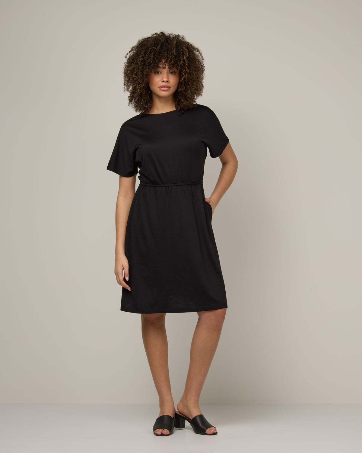 Model wearing Brooklyn Reversible Dress in Black. Brooklyn Reversible Dress is a merino wool short sleeve, reversible, knee length fit & flare dress with pockets available in sizes XS-3X Regular, XS-XL Long.