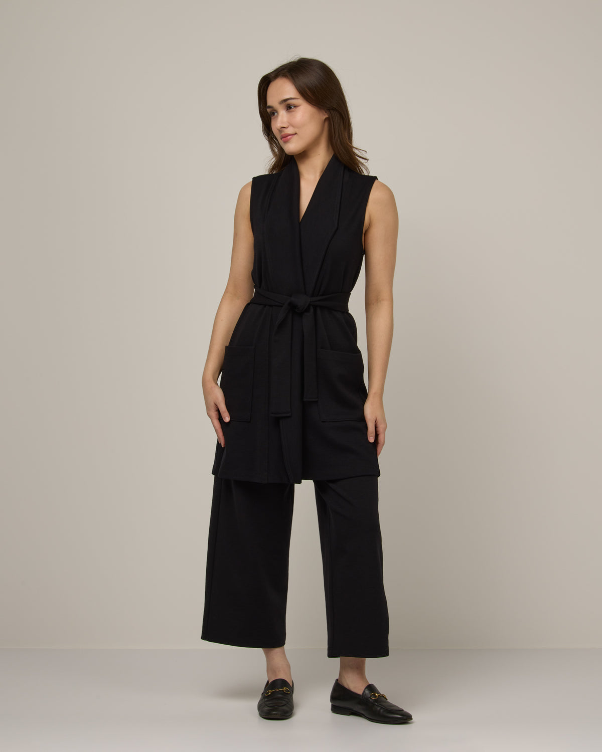 Model wearing Dylan Belted Vest in Black. Dylan Belted Vest is a merino wool sleevelessvest with pockets available in sizes XS-3X.