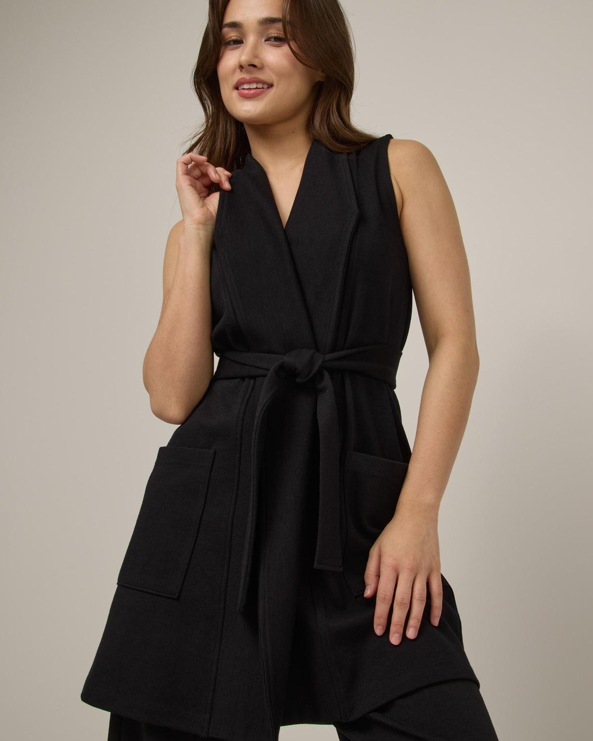 Model wearing Dylan Belted Vest in Black. Dylan Belted Vest is a merino wool sleevelessvest with pockets available in sizes XS-3X.