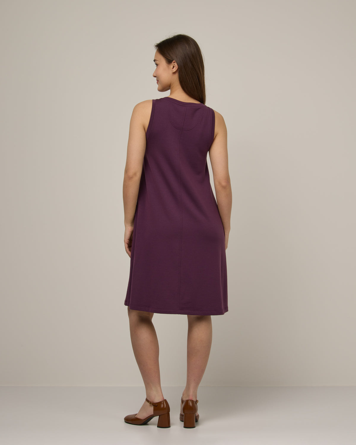 Model wearing Sierra Tank Dress in Marionberry, a dark berry purple color. Sierra Tank Dress is a merino wool sleeveless, crew neck, knee length swing dress with pockets available in sizes XS-3X Regular, XS-3X Long.