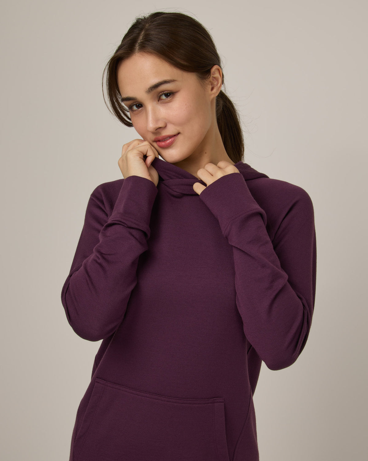 Model wearing Everett Hoodie Tunic in Marionberry, a dark berry purple color. Everett Hoodie Tunic is a merino wool long sleeve, crew neck, Tunic fitted sweatshirt with pockets available in sizes XS-3X.