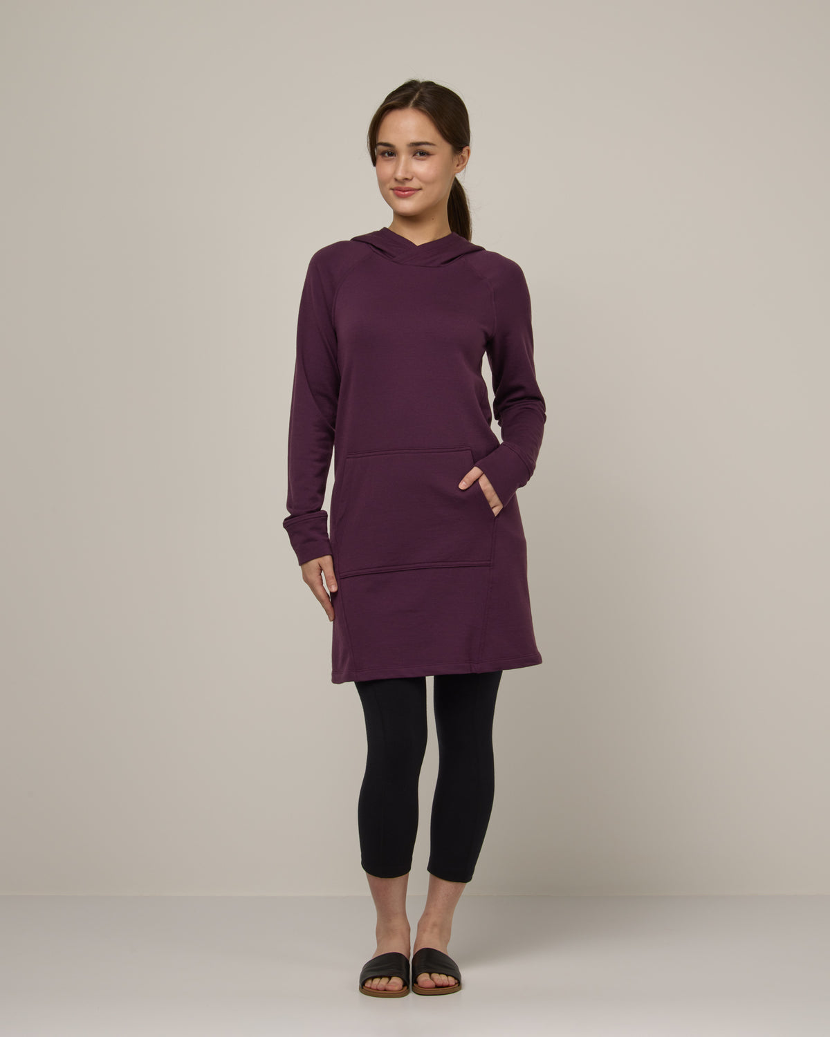 Model wearing Everett Hoodie Tunic in Marionberry, a dark berry purple color. Everett Hoodie Tunic is a merino wool long sleeve, crew neck, Tunic fitted sweatshirt with pockets available in sizes XS-3X.