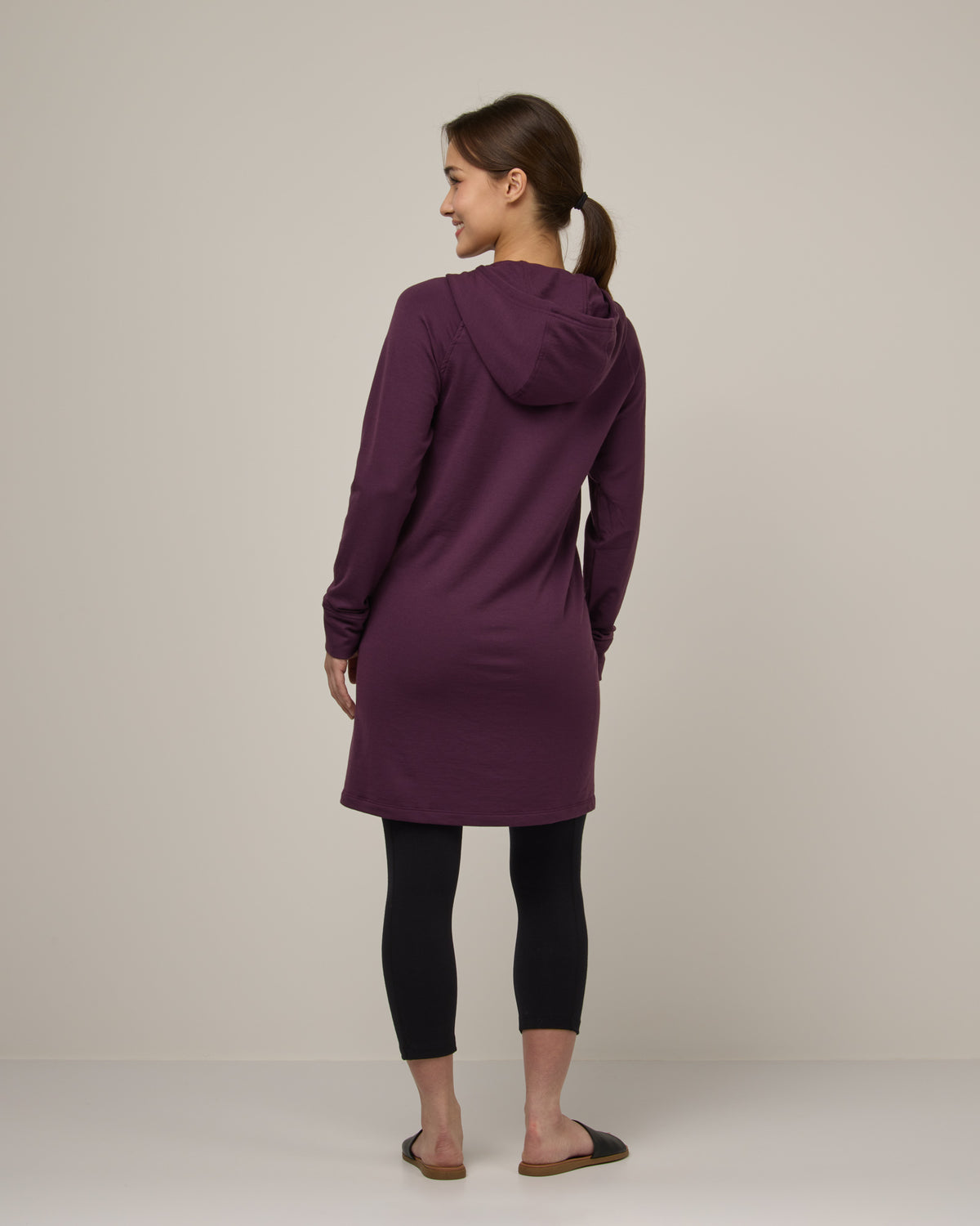 Model wearing Everett Hoodie Tunic in Marionberry, a dark berry purple color. Everett Hoodie Tunic is a merino wool long sleeve, crew neck, Tunic fitted sweatshirt with pockets available in sizes XS-3X.