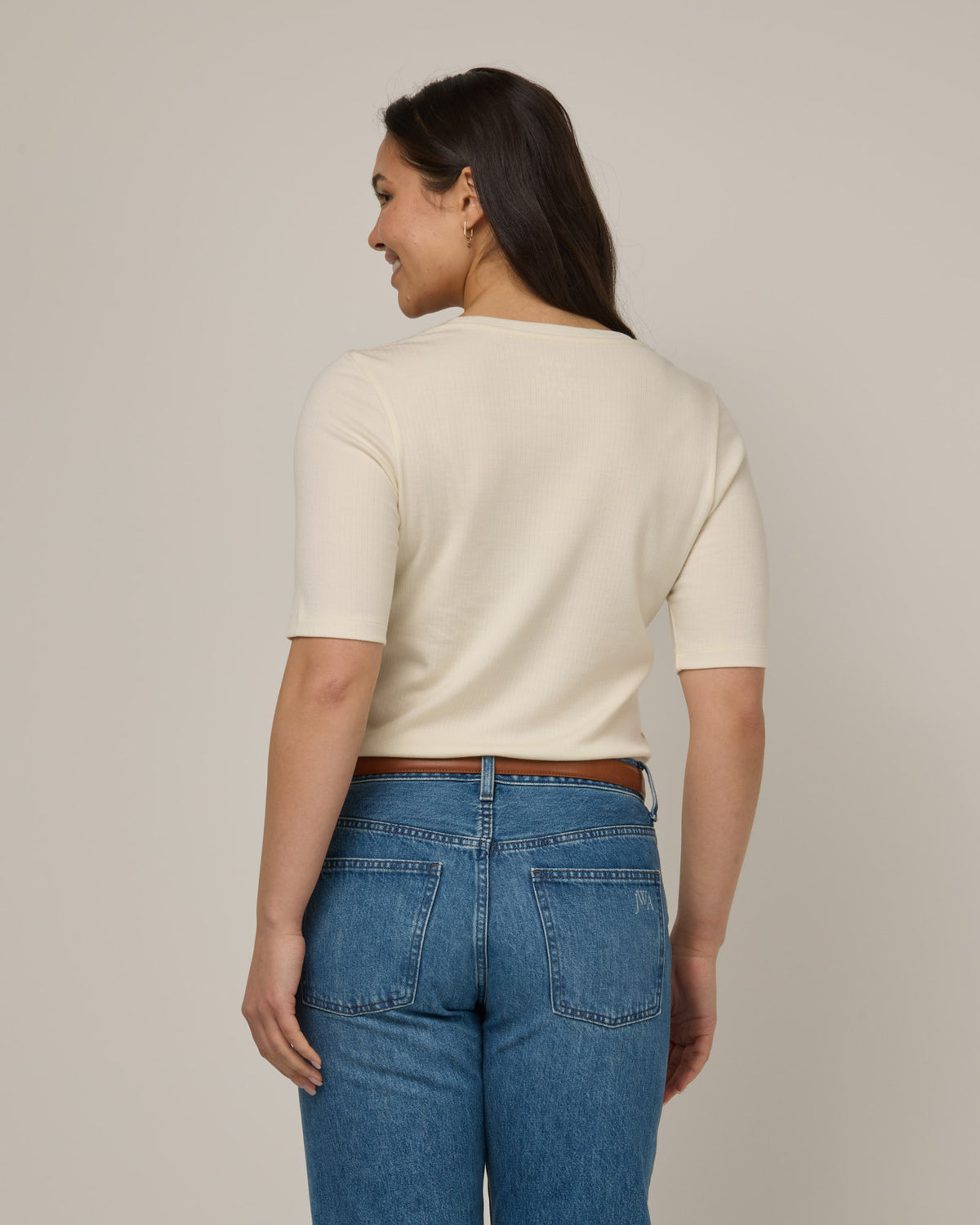 Model wearing Celine Ribbed Elbow Sleeve Tee in Natural White, an off-white cream color. Celine Ribbed Elbow Sleeve Tee is a merino wool short sleeve, scoop neck, slim fit tee available in sizes XS-3X.
