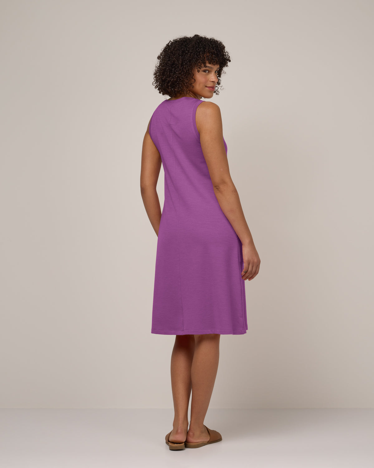 Model wearing Sierra Tank Dress in Purple Pansy, a bright, saturated purple color. Sierra Tank Dress is a merino wool sleeveless, crew neck, knee length swing dress with pockets available in sizes XS-3X Regular, XS-3X Long, XS-XL Petite.