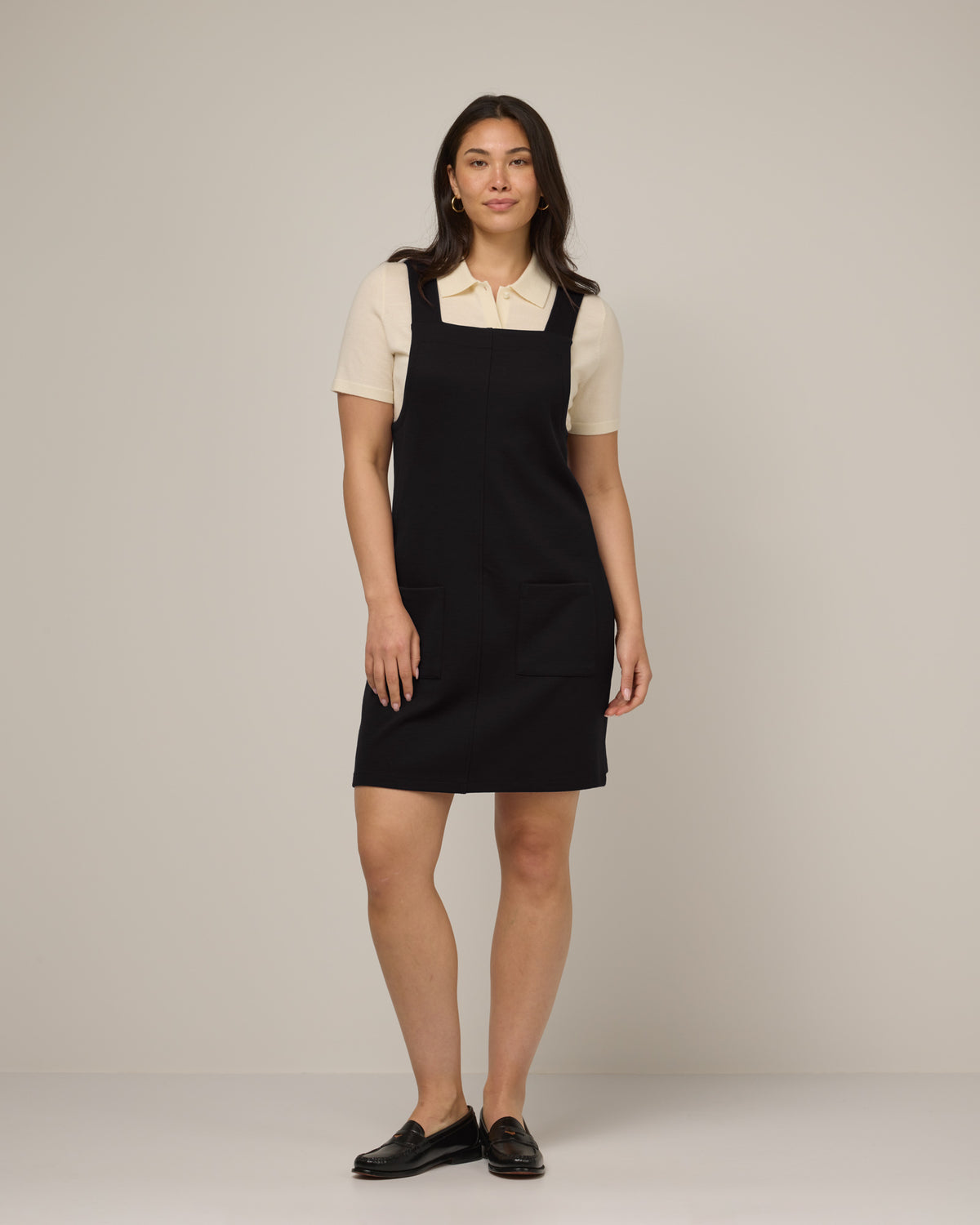 Model wearing Goldie Pinafore Dress in Black. Goldie Pinafore Dress is a merino wool sleeveless, square neck, knee length shift dress with pockets available in sizes XS-3X.