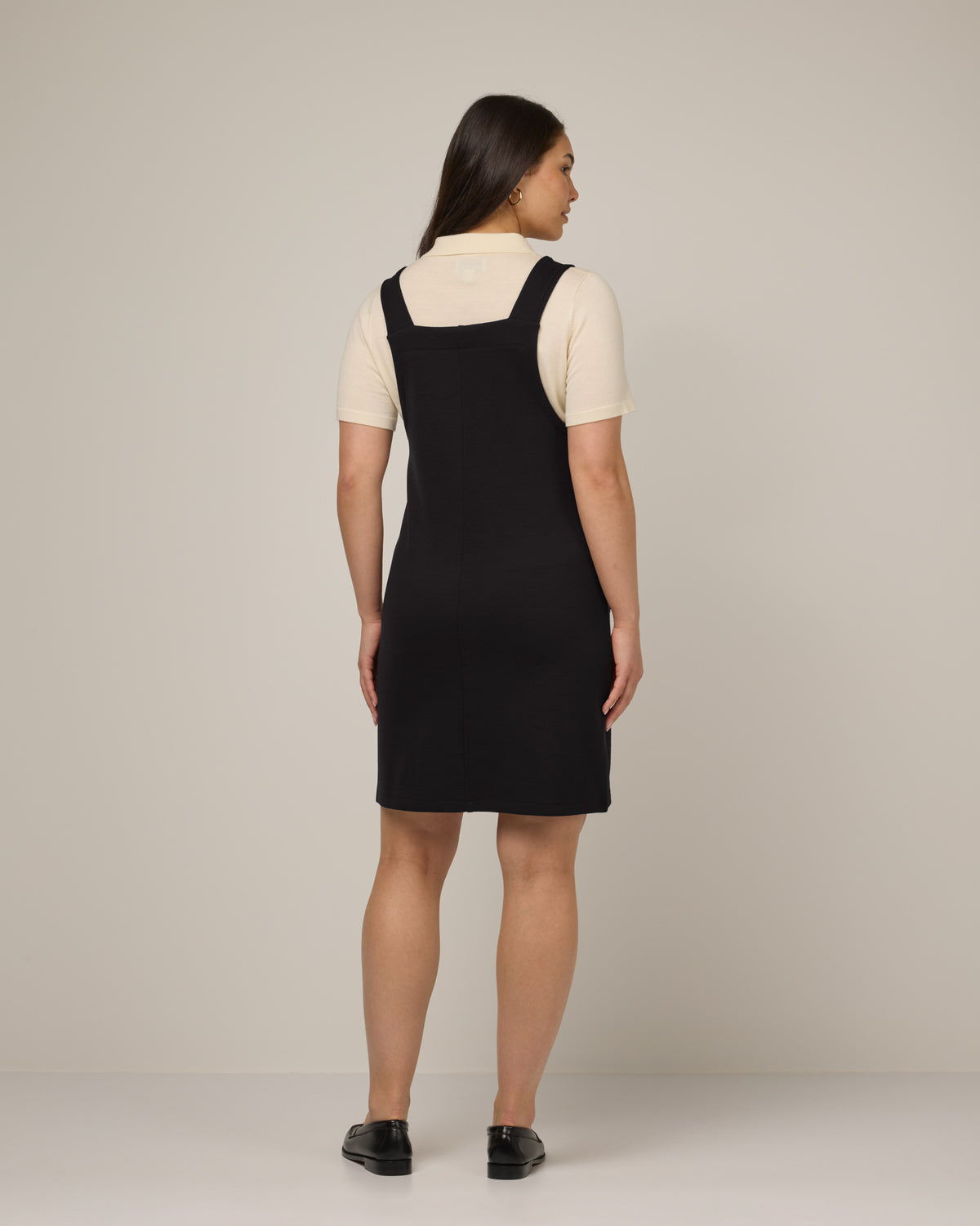Model wearing Goldie Pinafore Dress in Black. Goldie Pinafore Dress is a merino wool sleeveless, square neck, knee length shift dress with pockets available in sizes XS-3X.