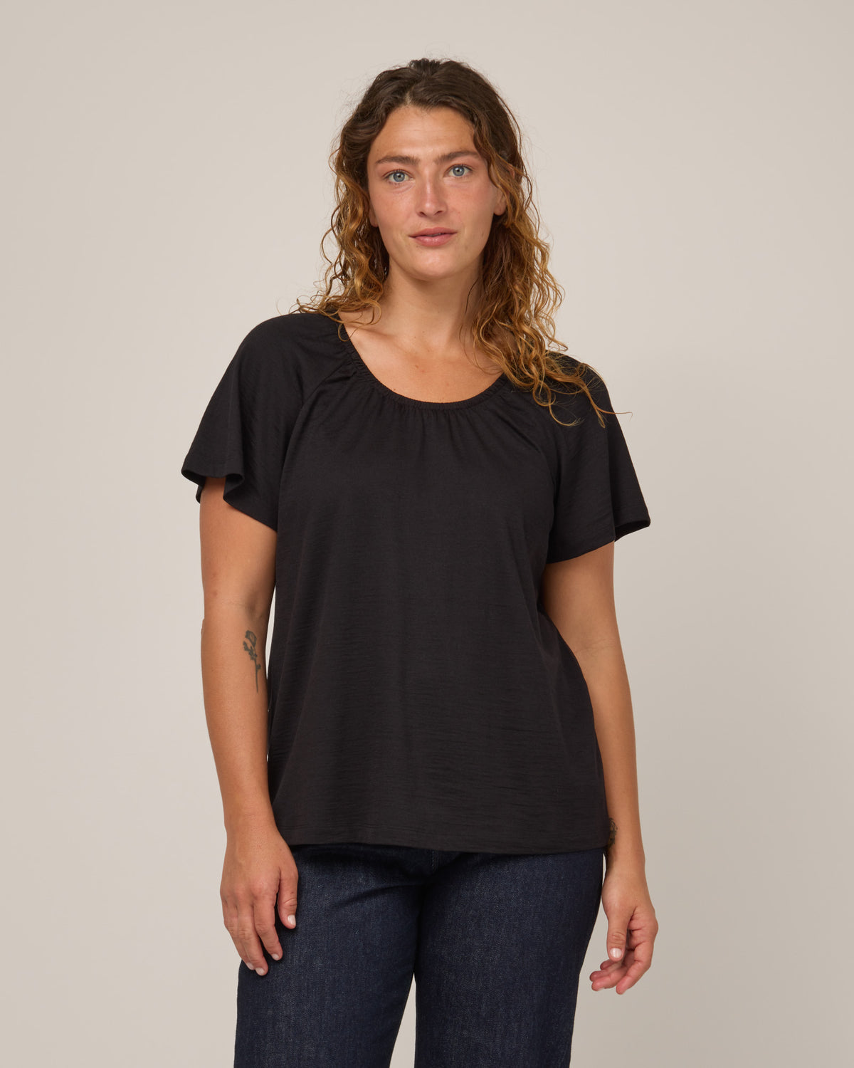 Model wearing Lilah Signature Gathered Neck Tee in Black. Lilah Signature Gathered Neck Tee is a merino wool short sleeve, scoop neck, relaxed fit tee available in sizes XS-3X.