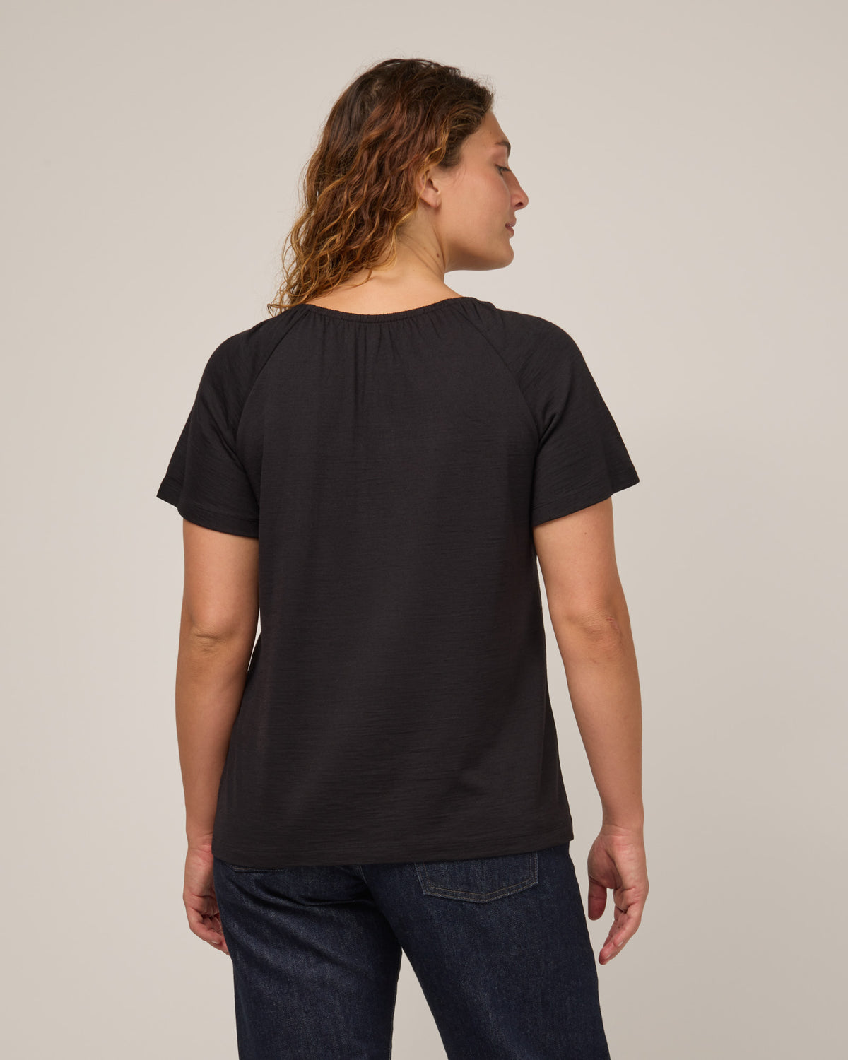 Model wearing Lilah Signature Gathered Neck Tee in Black. Lilah Signature Gathered Neck Tee is a merino wool short sleeve, scoop neck, relaxed fit tee available in sizes XS-3X.
