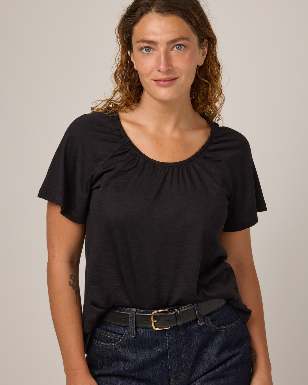 Model wearing Lilah Signature Gathered Neck Tee in Black. Lilah Signature Gathered Neck Tee is a merino wool short sleeve, scoop neck, relaxed fit tee available in sizes XS-3X.