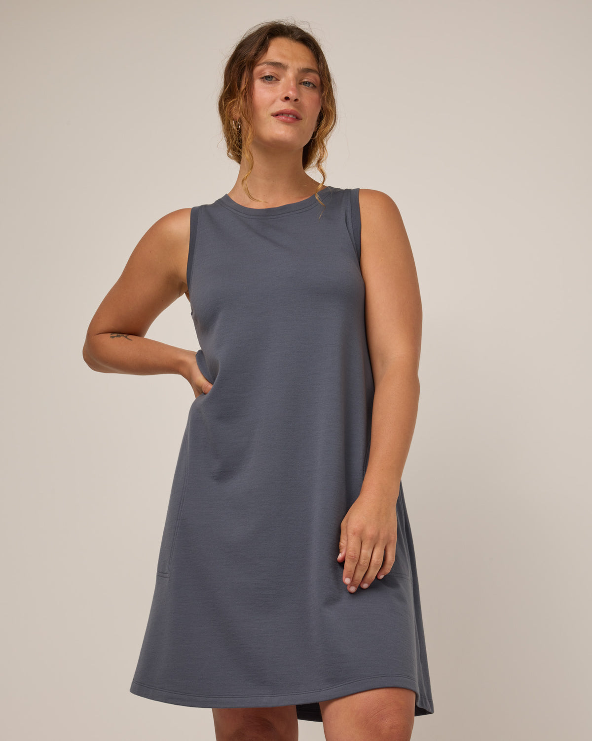 Model wearing Sierra Tank Dress in Odyssey Gray, a neutral purplish-gray color. Sierra Tank Dress is a merino wool sleeveless, crew neck, knee length swing dress with pockets available in sizes XS-3X Regular, XS-3X Long.