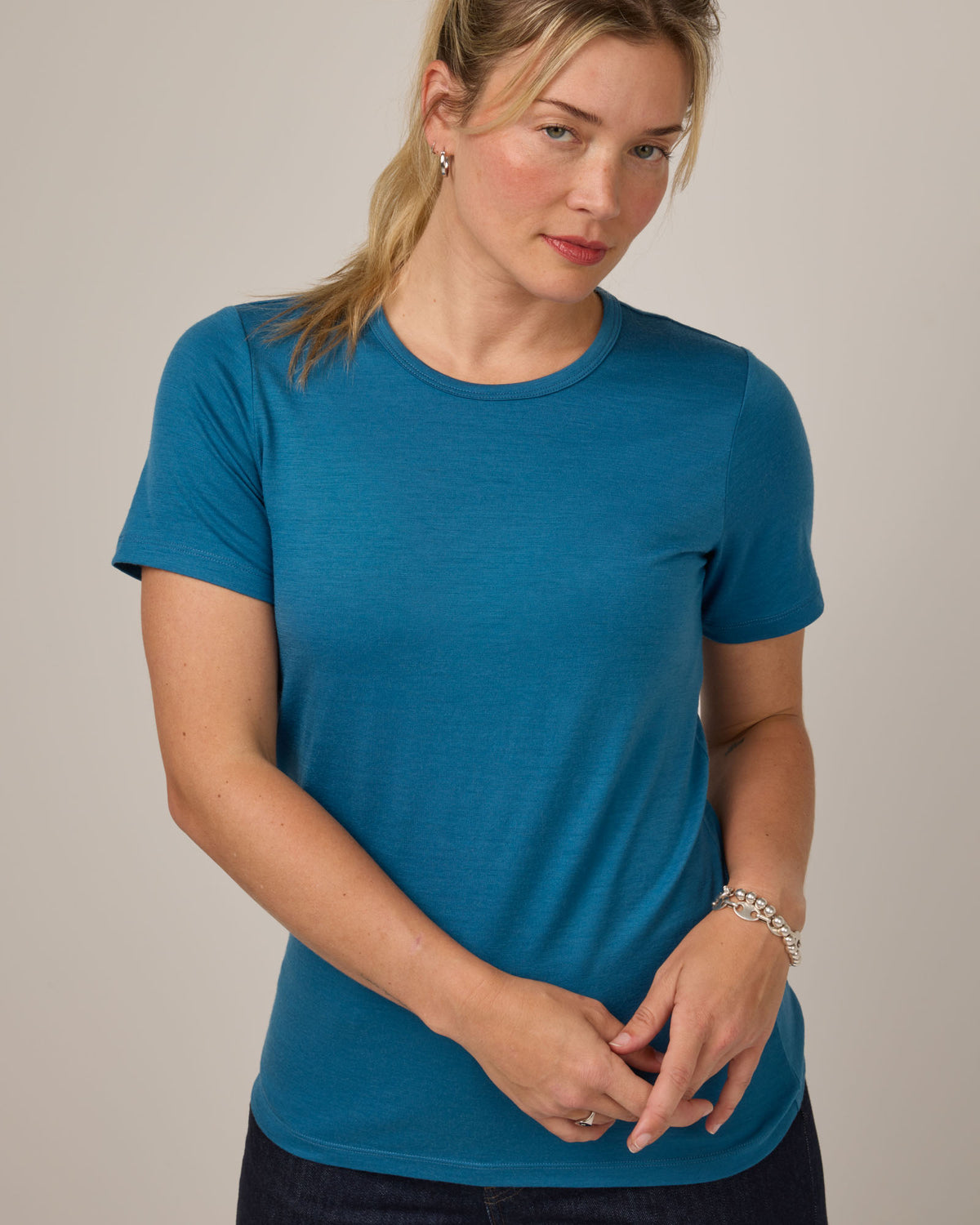 Model wearing Cara 100% Wool Fitted Tee in Ocean Teal, a medium blue-green color. Cara 100% Wool Fitted Tee is a merino wool short sleeve, crew neck, slim fit tee available in sizes XS-3X.