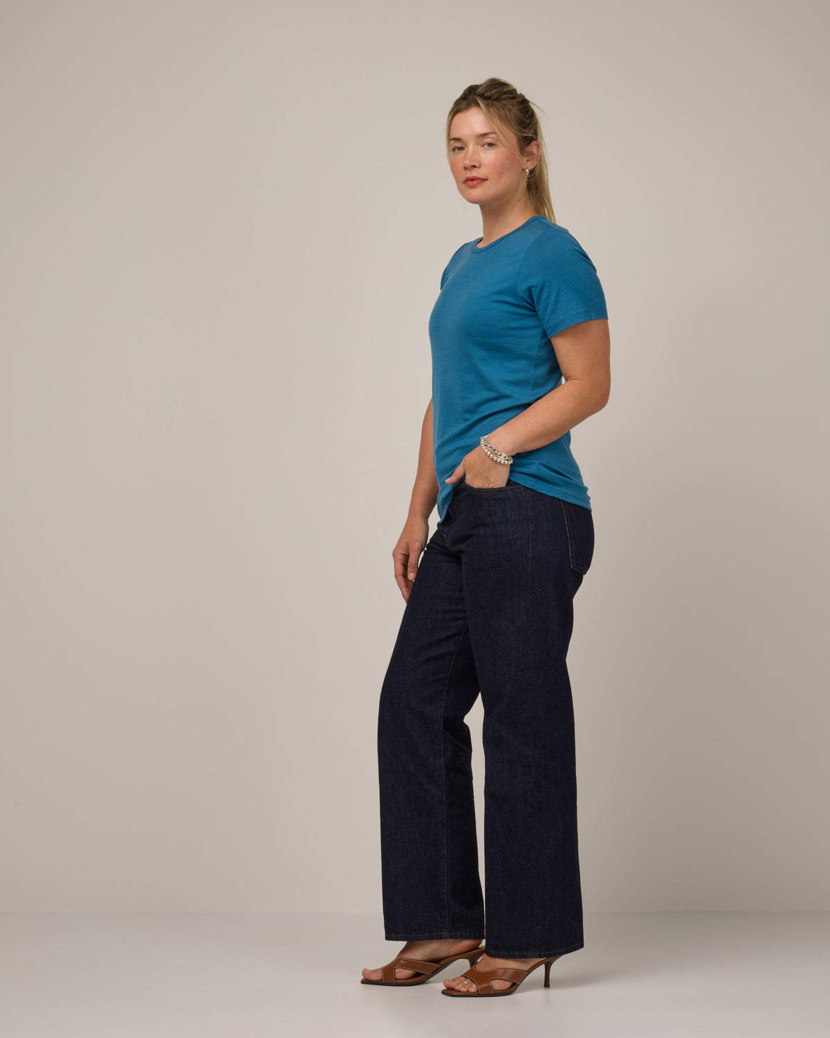 Model wearing Cara 100% Wool Fitted Tee in Ocean Teal, a medium blue-green color. Cara 100% Wool Fitted Tee is a merino wool short sleeve, crew neck, slim fit tee available in sizes XS-3X.