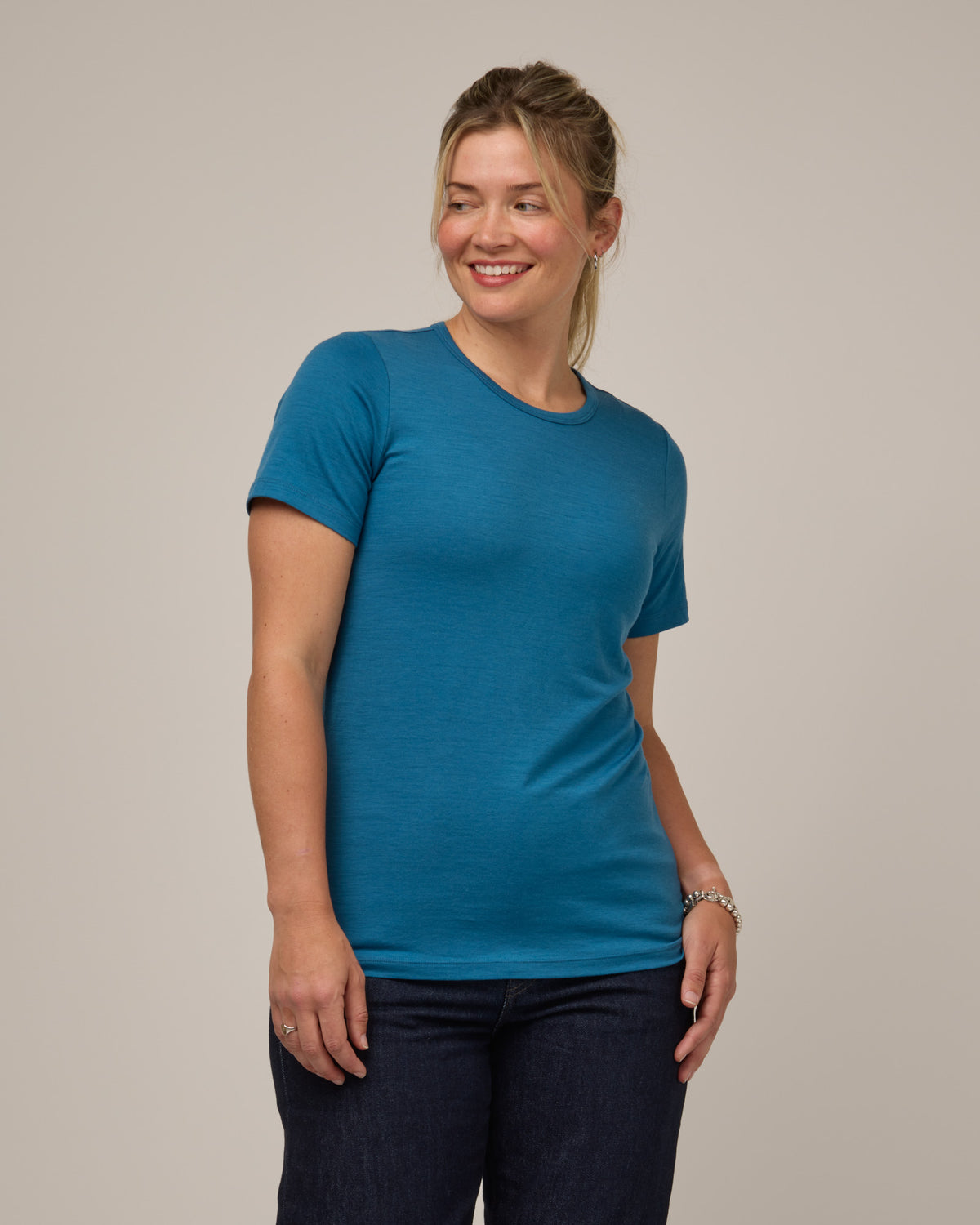 Model wearing Cara 100% Wool Fitted Tee in Ocean Teal, a medium blue-green color. Cara 100% Wool Fitted Tee is a merino wool short sleeve, crew neck, slim fit tee available in sizes XS-3X.