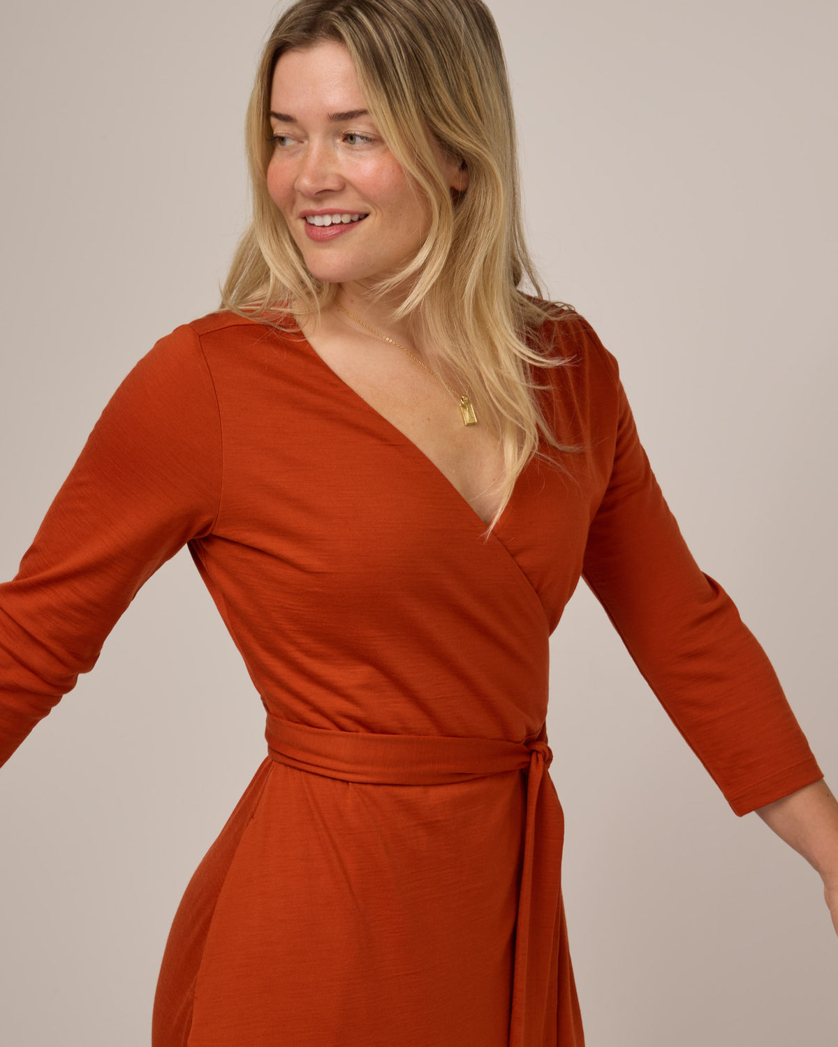 Model wearing Alana Wrap Dress in Terracotta, a saturated red-orange color. Alana Wrap Dress is a merino wool long sleeve, v-neck, midi fit & flare dress with pockets available in sizes XS-3X.
