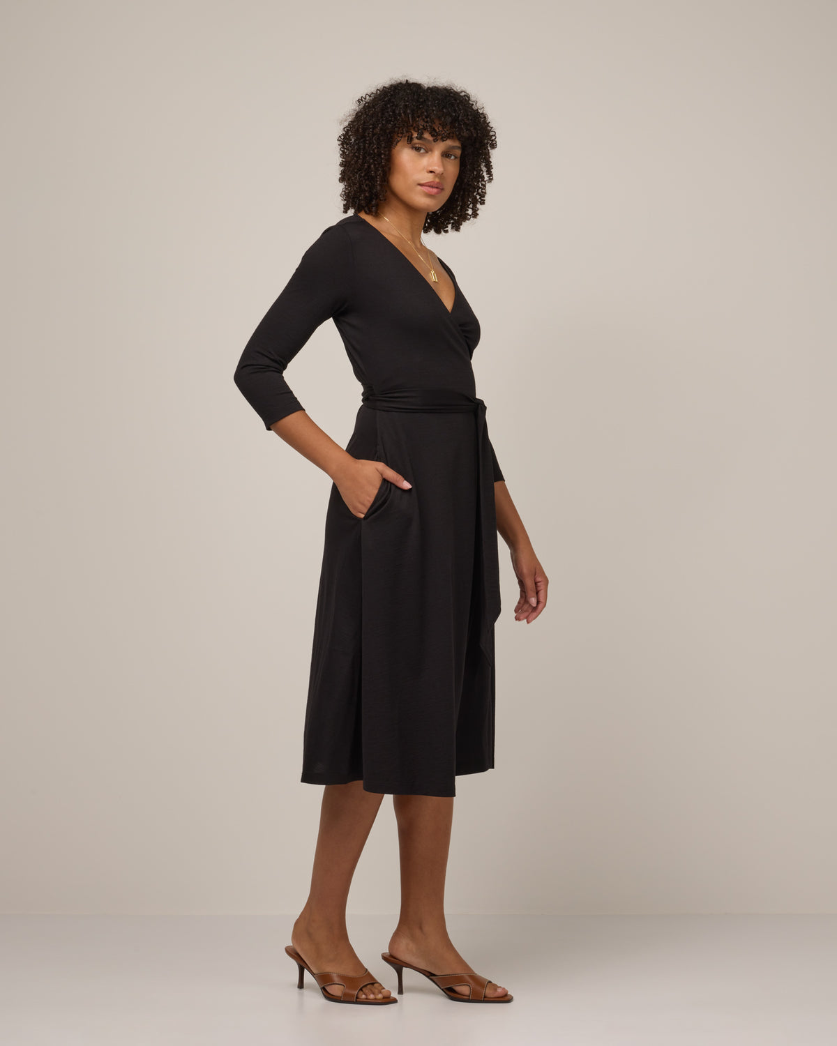 Model wearing Alana Wrap Dress in Black. Alana Wrap Dress is a merino wool long sleeve, v-neck, midi fit & flare dress with pockets available in sizes XS-3X.