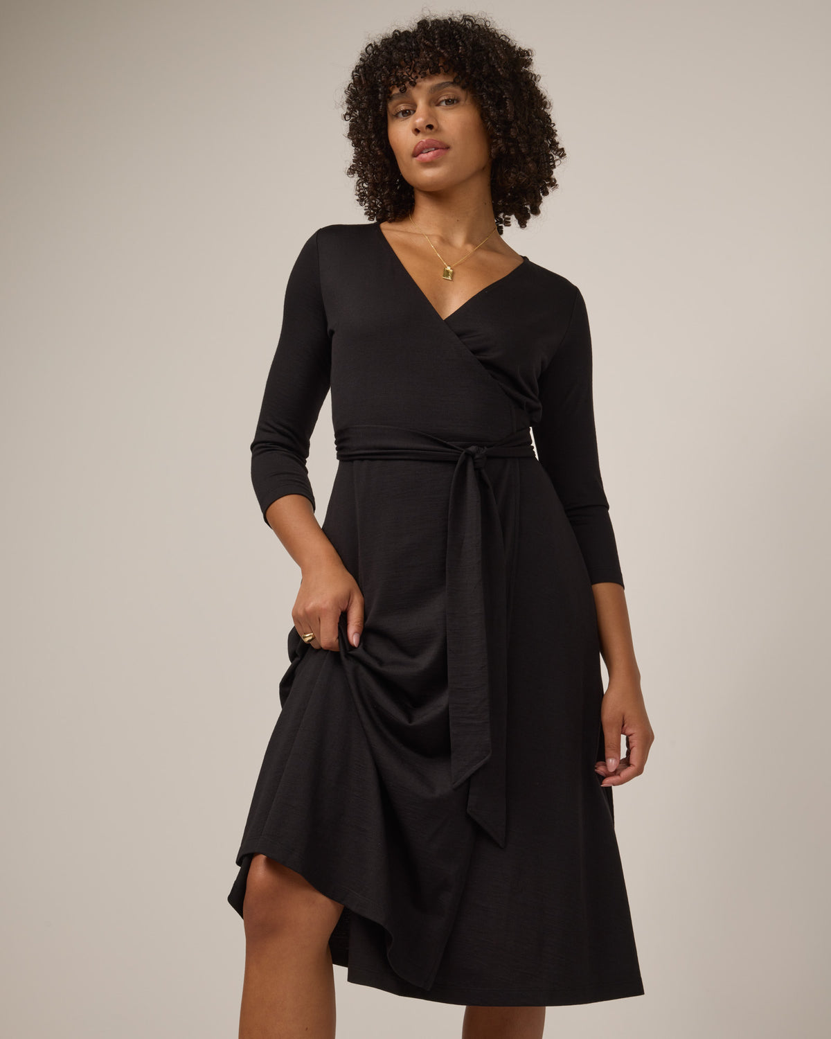 Model wearing Alana Wrap Dress in Black. Alana Wrap Dress is a merino wool long sleeve, v-neck, midi fit & flare dress with pockets available in sizes XS-3X.