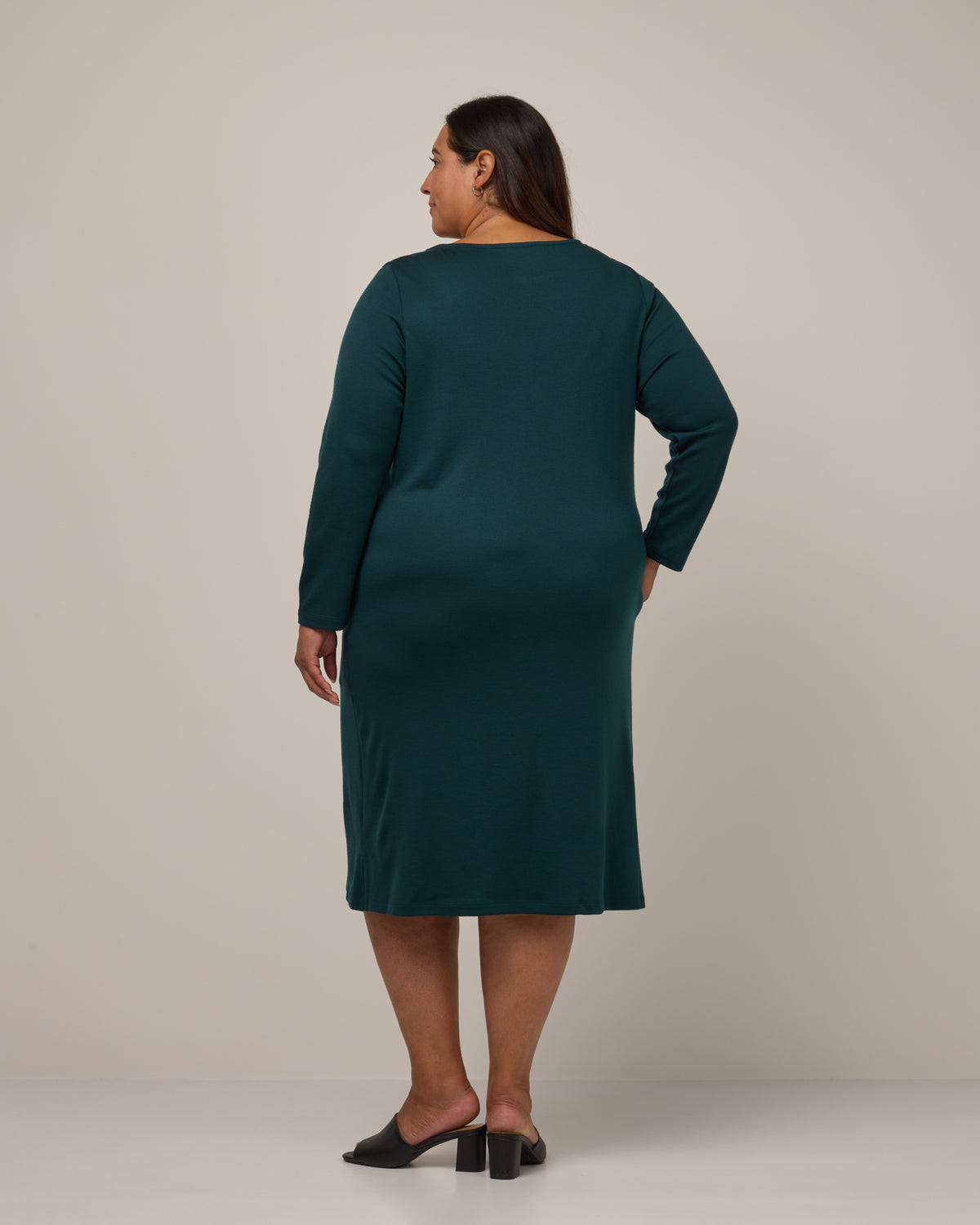 Model wearing Margo Shift Dress in Pine, a saturated forest green color. Margo Shift Dress is a merino wool long sleeve, boatneck, knee length shift dress with pockets available in sizes XS-3X Regular, S-3X Long.