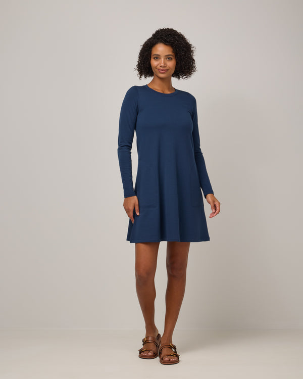 Model wearing Eliza Swing Dress in Marine Blue, a deep royal blue color. Eliza Swing Dress is a merino wool long sleeve, crew neck, knee length swing dress with pockets available in sizes XS-3X Regular, XS-3X Long.