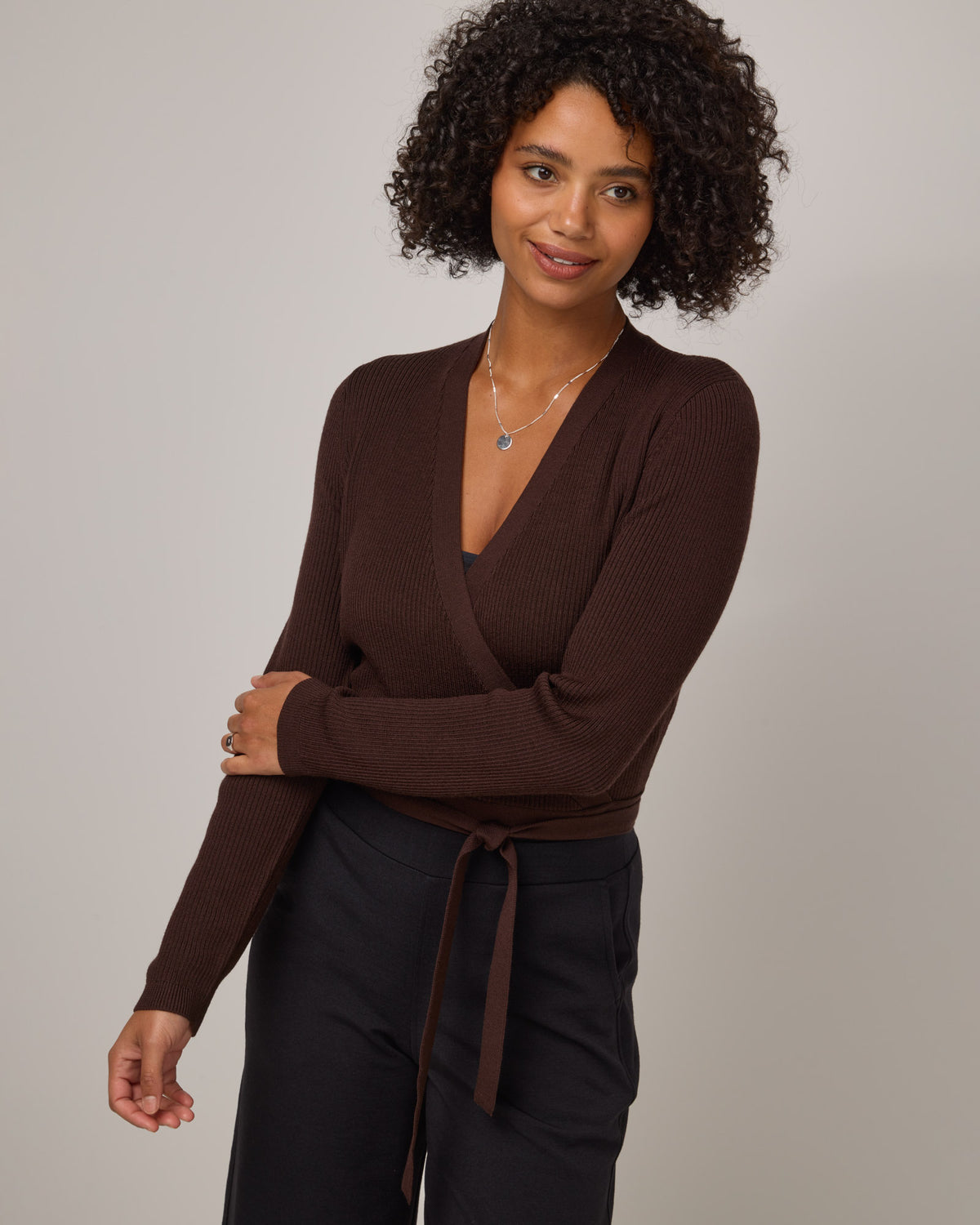 Model wearing Adeline Wrap Sweater in Espresso, a dark brown color. Adeline Wrap Sweater is a merino wool long sleeve, v-neck, regular fit sweater available in sizes XS-3X.