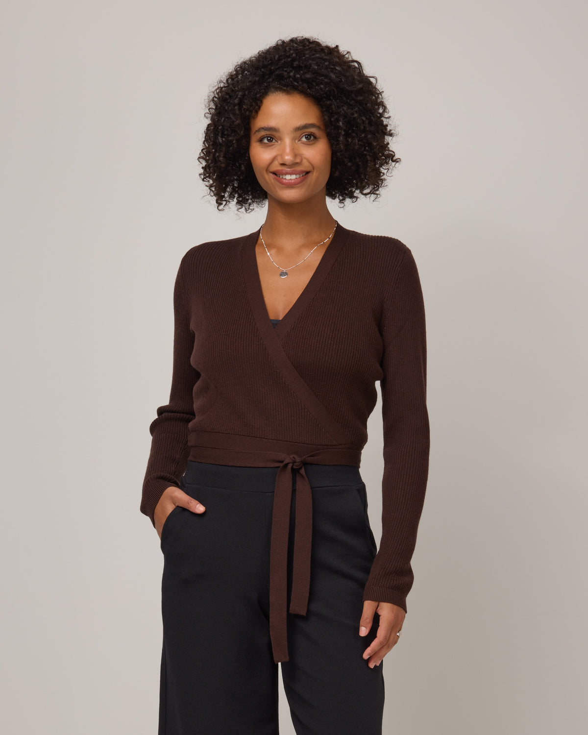 Model wearing Adeline Wrap Sweater in Espresso, a dark brown color. Adeline Wrap Sweater is a merino wool long sleeve, v-neck, regular fit sweater available in sizes XS-3X.