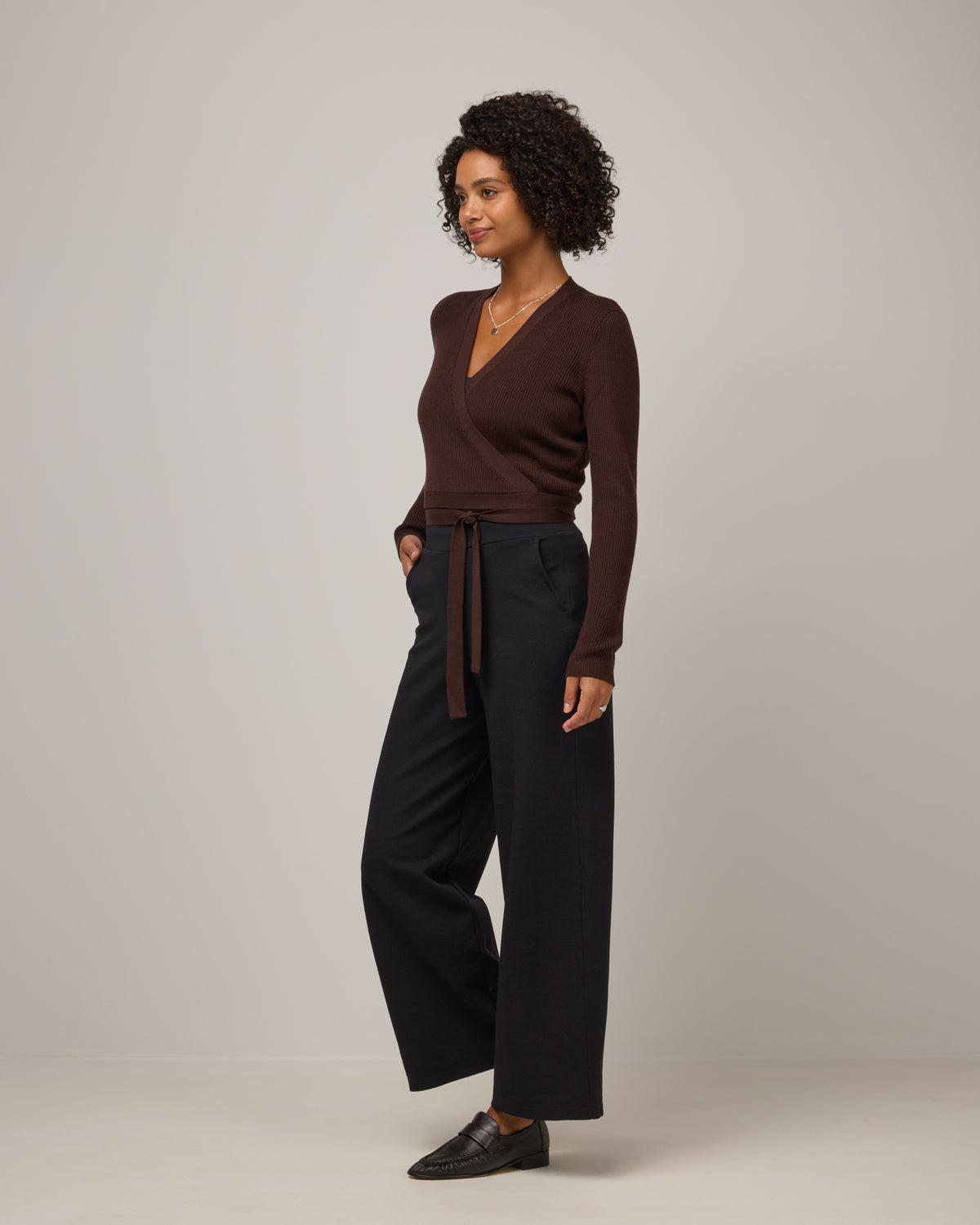 Model wearing Adeline Wrap Sweater in Espresso, a dark brown color. Adeline Wrap Sweater is a merino wool long sleeve, v-neck, regular fit sweater available in sizes XS-3X.