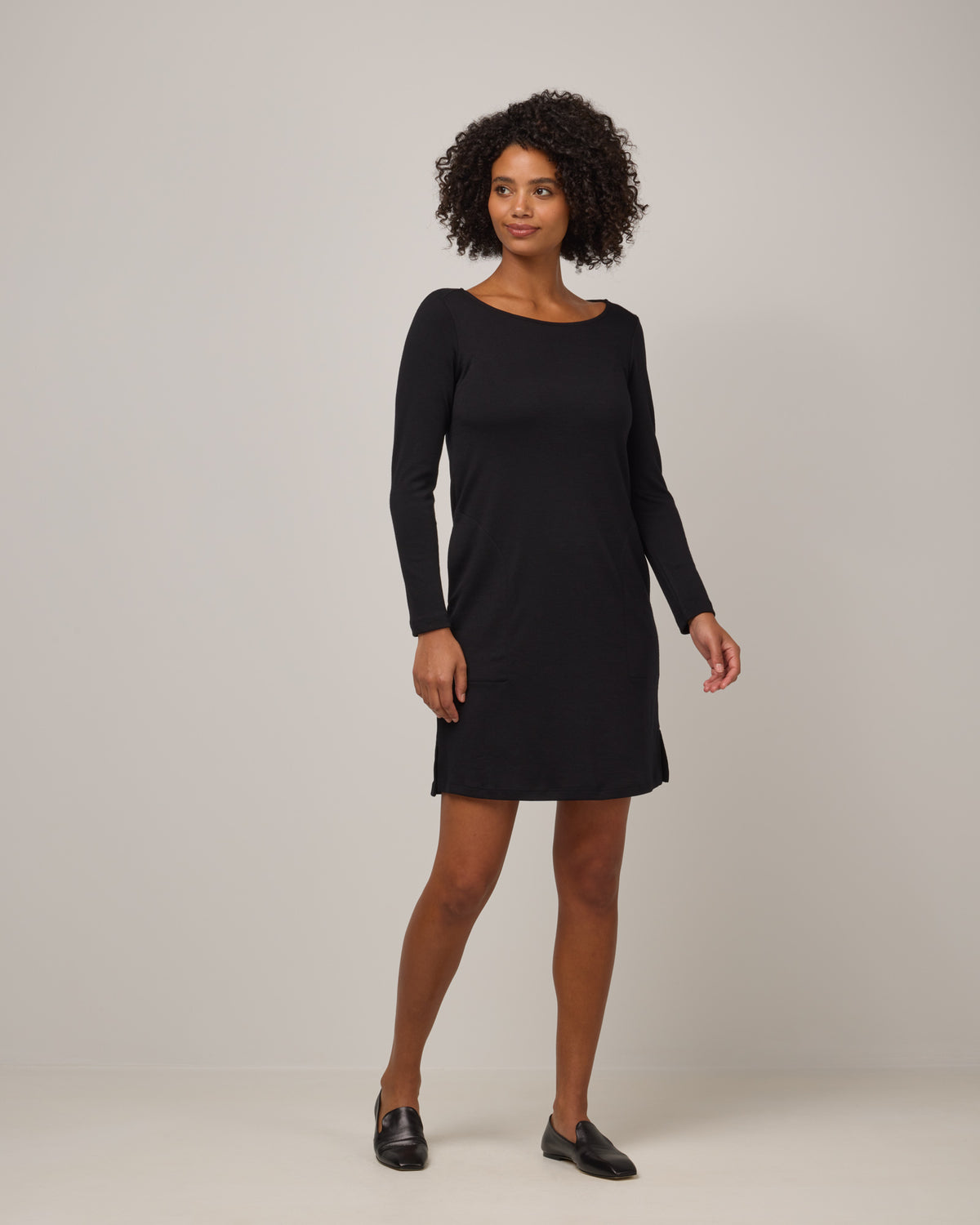 Model wearing Margo Shift Dress in Black. Margo Shift Dress is a merino wool long sleeve, boatneck, knee length shift dress with pockets available in sizes XS-3X Regular, S-3X Long.