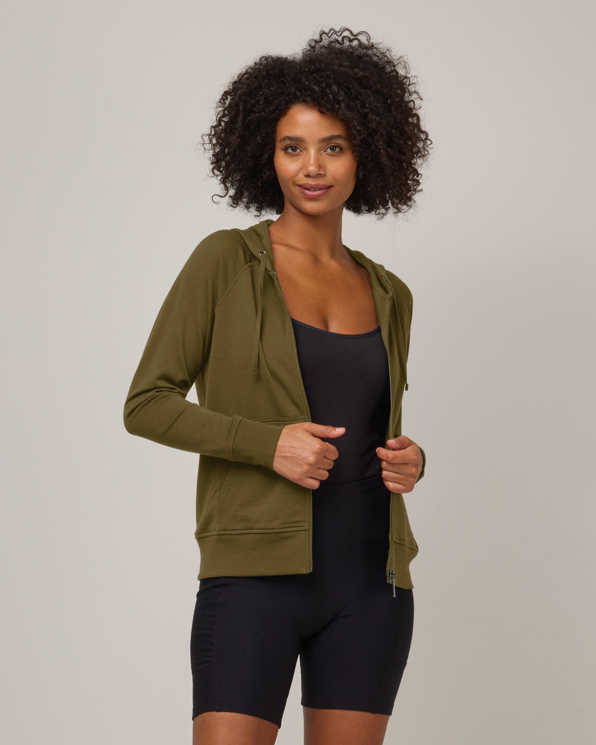 Model wearing Aspen Full-Zip Hoodie in Olive. Aspen Full-Zip Hoodie is a merino wool long sleeve zip hoodie with pockets available in sizes XS-3X.