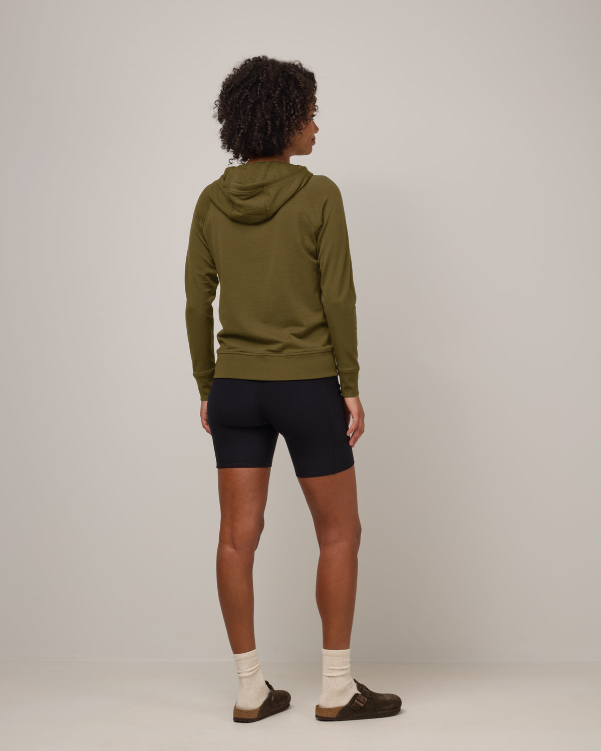 Model wearing Aspen Full-Zip Hoodie in Olive. Aspen Full-Zip Hoodie is a merino wool long sleeve zip hoodie with pockets available in sizes XS-3X.
