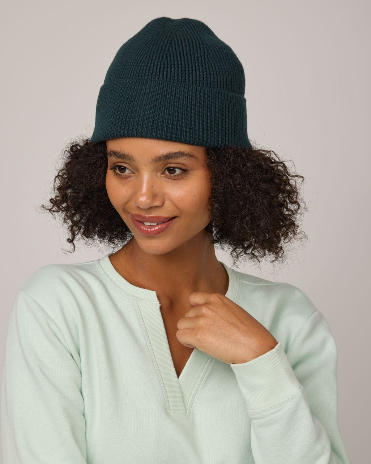 Model wearing Rory Ribbed Beanie in Pine, a saturated forest green color. Rory Ribbed Beanie is a merino wool hat available in one size.