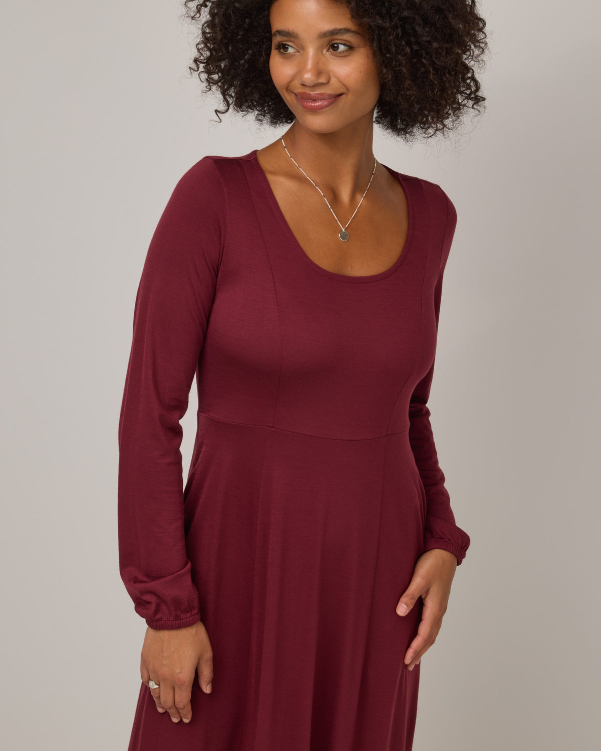 Model wearing Ahna Empire Waist Dress in Burgundy. Ahna Empire Waist Dress is a merino wool long sleeve, square neck, maxi fit & flare dress with pockets available in sizes XS-3X.