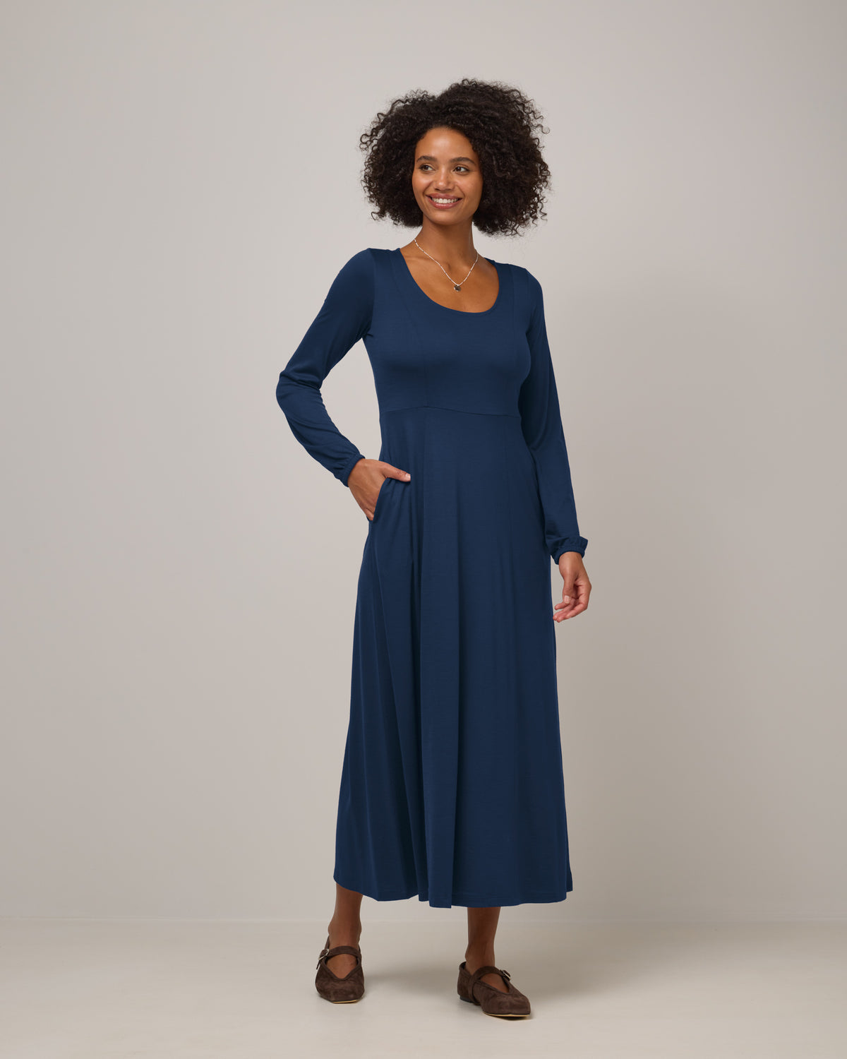Model wearing Ahna Empire Waist Dress in Marine Blue, a deep royal blue color. Ahna Empire Waist Dress is a merino wool long sleeve, square neck, maxi fit & flare dress with pockets available in sizes XS-3X.