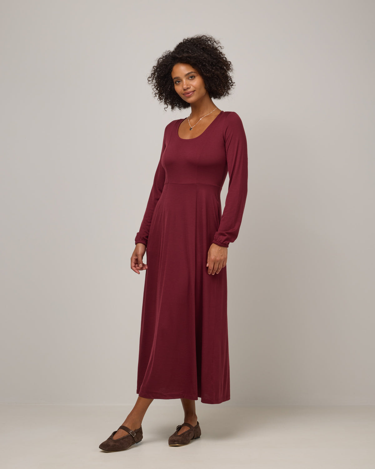 Model wearing Ahna Empire Waist Dress in Burgundy. Ahna Empire Waist Dress is a merino wool long sleeve, square neck, maxi fit & flare dress with pockets available in sizes XS-3X.