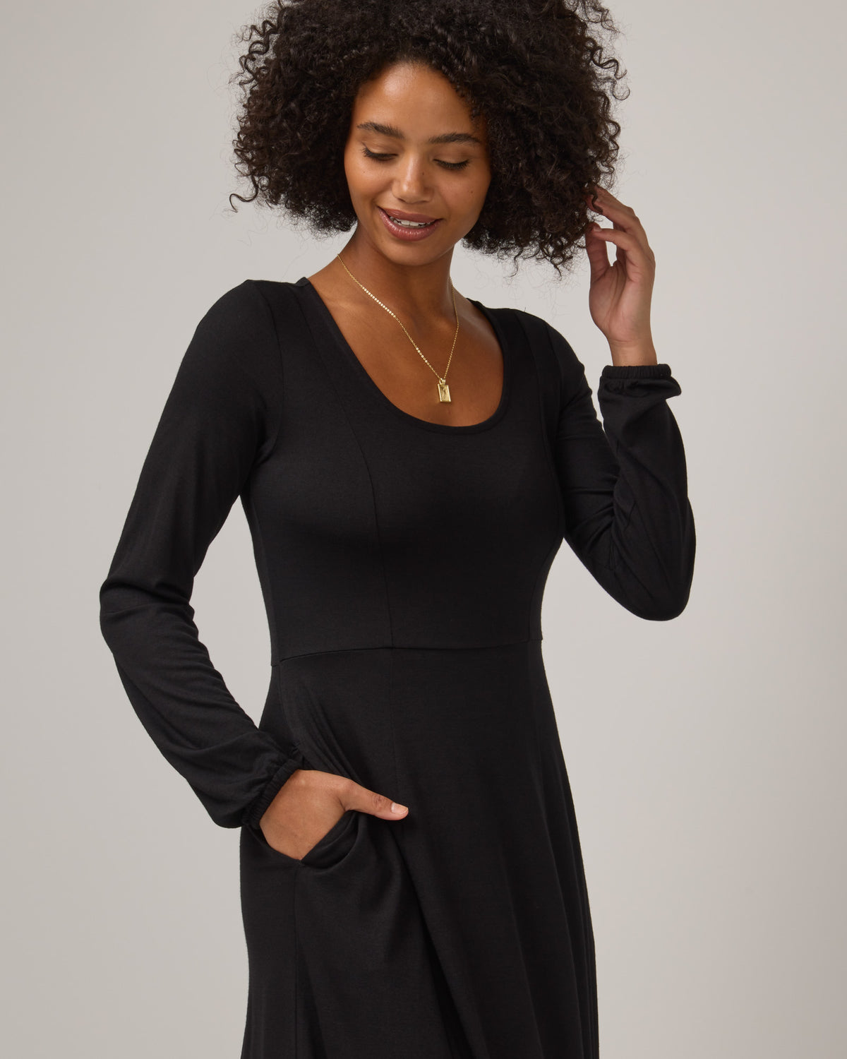 Model wearing Ahna Empire Waist Dress in Black. Ahna Empire Waist Dress is a merino wool long sleeve, square neck, maxi fit & flare dress with pockets available in sizes XS-3X.