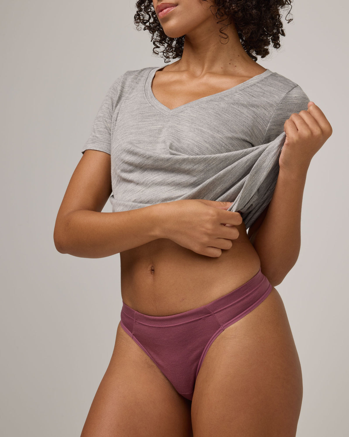 Model wearing Roam Thong in Rosewood, a muted, dark pink-purple color . Roam Thong is a merino wool underwear available in sizes XS-3X.