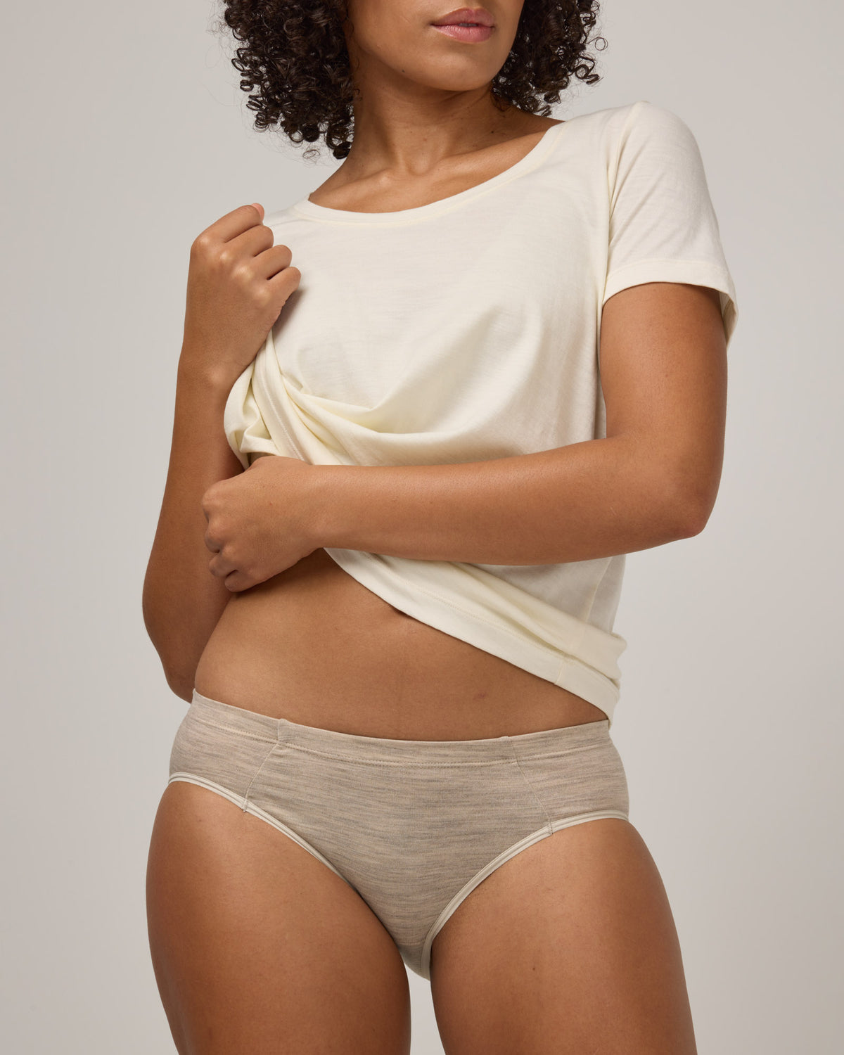 Model wearing Roam Bikini in Oatmeal Heather, a soft heathered cream color. Roam Bikini is a merino wool underwear available in sizes XS-3X.