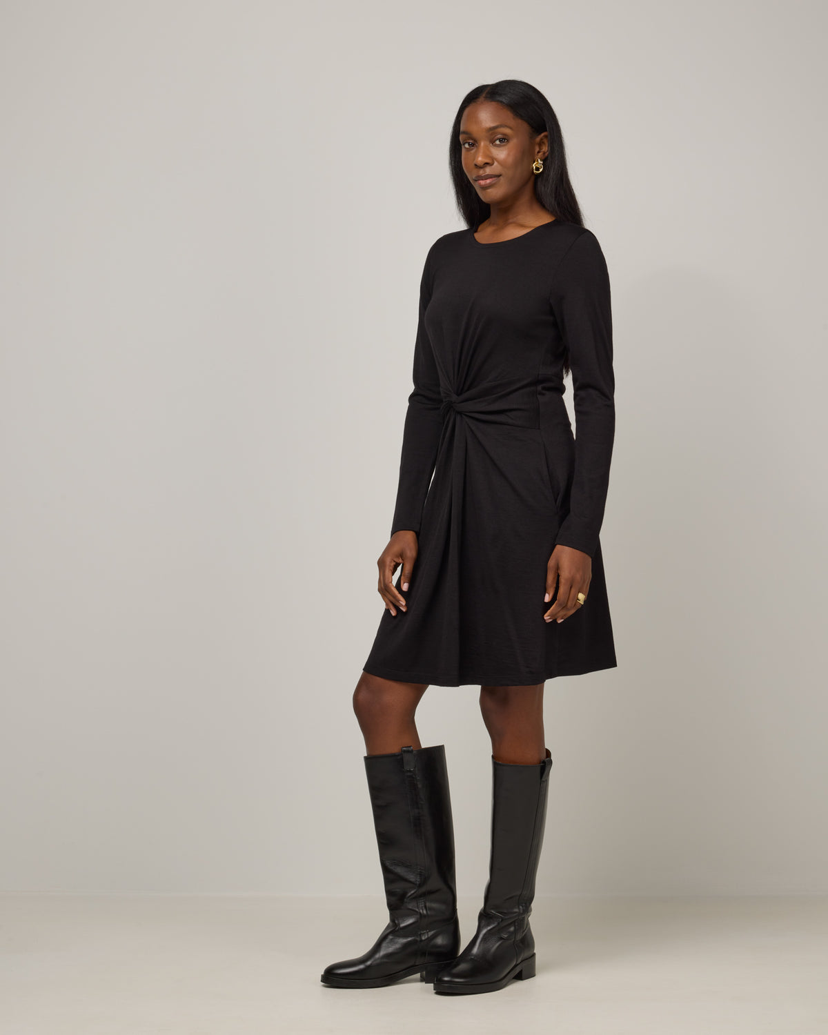 Model wearing Nova Twist Front Dress in Black. Nova Twist Front Dress is a merino wool long sleeve, crew neck, knee length fit & flare dress with pockets available in sizes XS-3X.