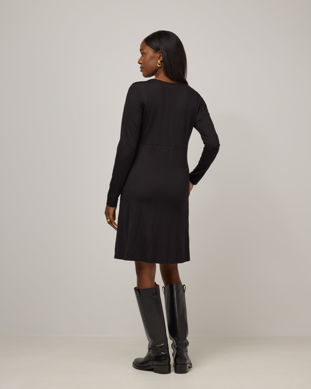 Model wearing Nova Twist Front Dress in Black. Nova Twist Front Dress is a merino wool long sleeve, crew neck, knee length fit & flare dress with pockets available in sizes XS-3X.